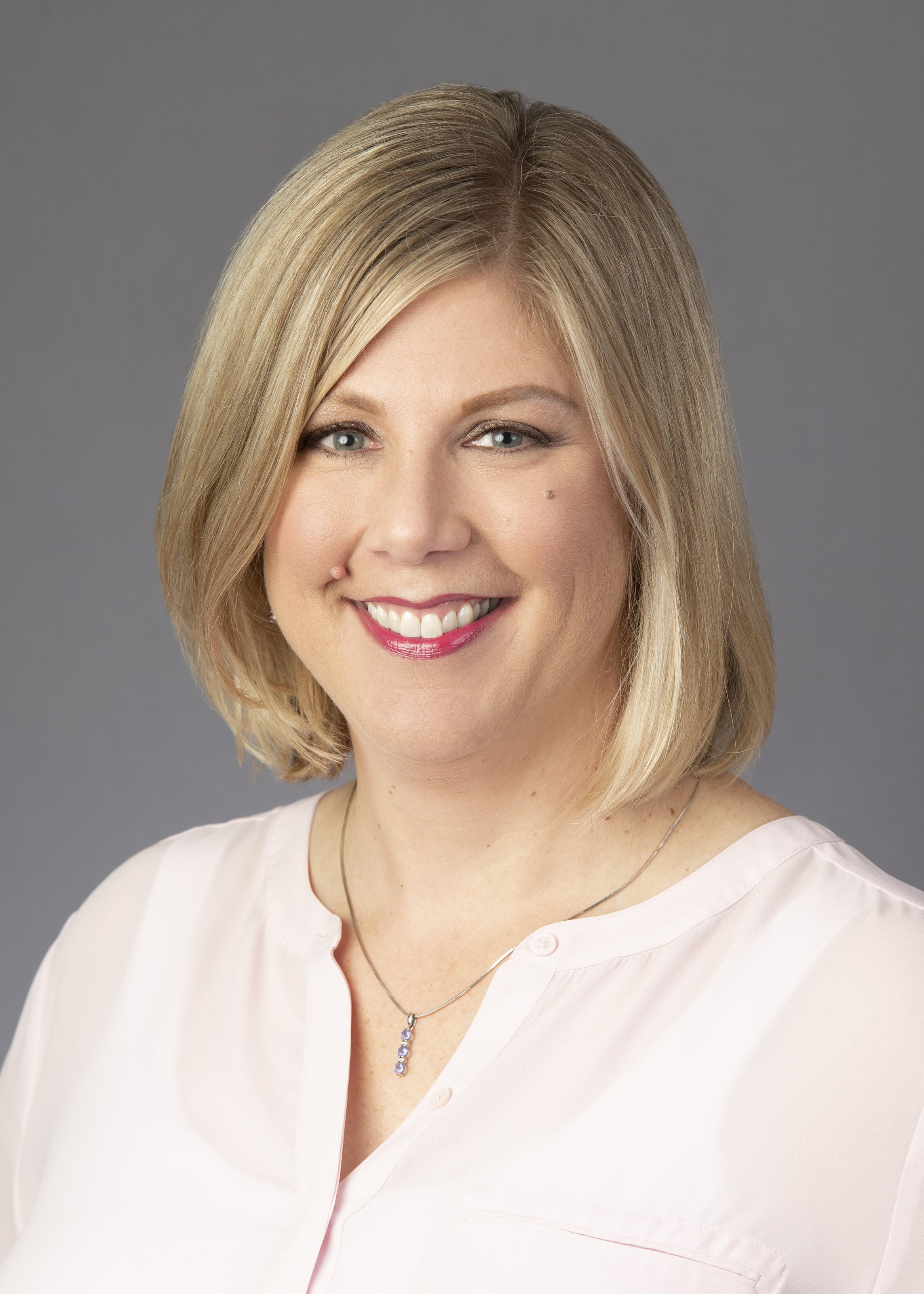 Business headshot in Chicago on grey backdrop. This head shot was in an accounting firm of a smiling blonde woman in a casual pink shirt.