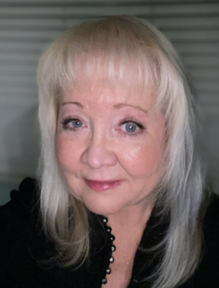 A woman with blonde hair and blue eyes smiling at the camera, wearing a black top with buttons.