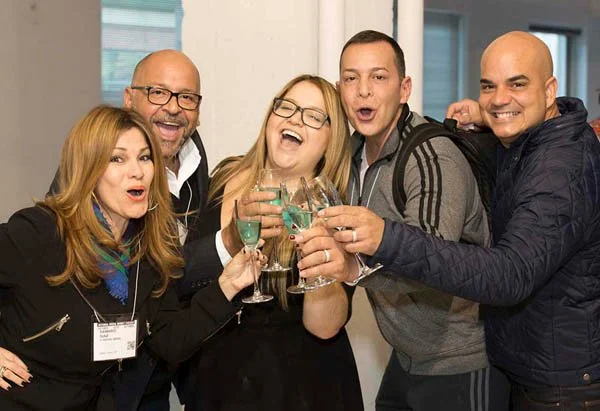 Group of five people celebrating and clinking glasses at a social gathering.