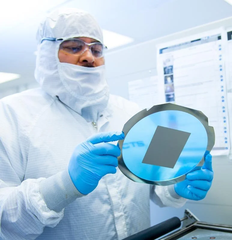 A scientist in protective gear holding a silicon wafer in a cleanroom environment.