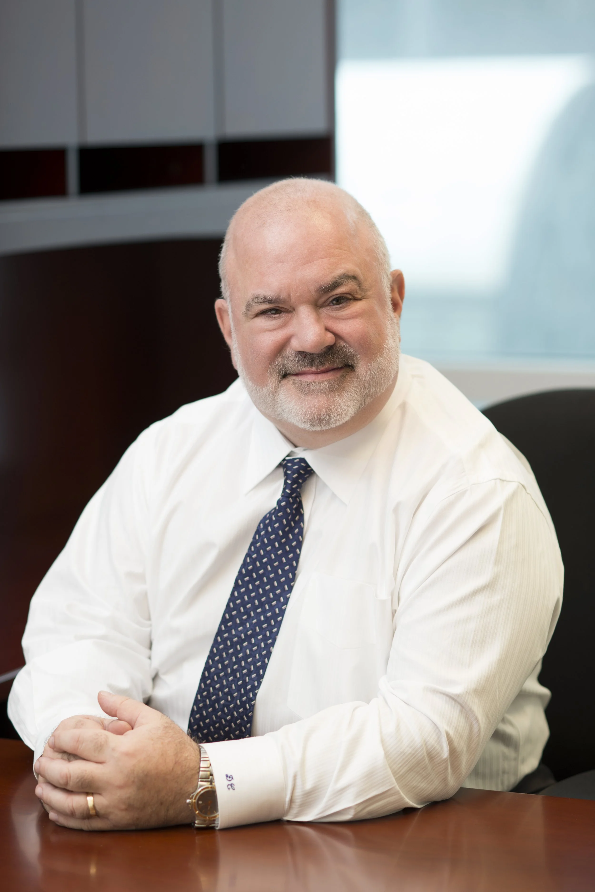 Chicago business portrait photography of an attorney at his desk with a blurred background with his hands folded wearing a white shirt and tie for an annual report 