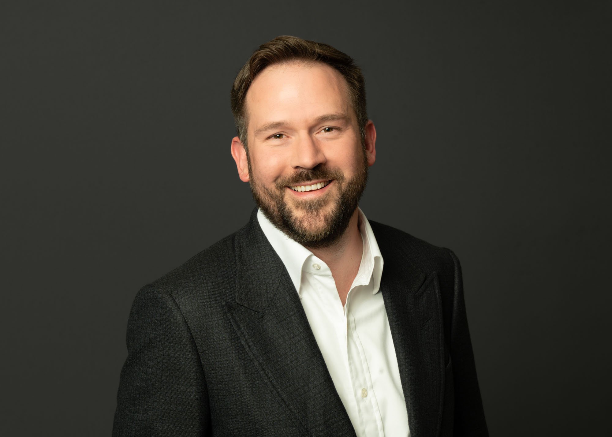 Professional headshot of a CEO in Chicago on a dark grey backdrop. This is in business attire as directed by the headshot photographer.