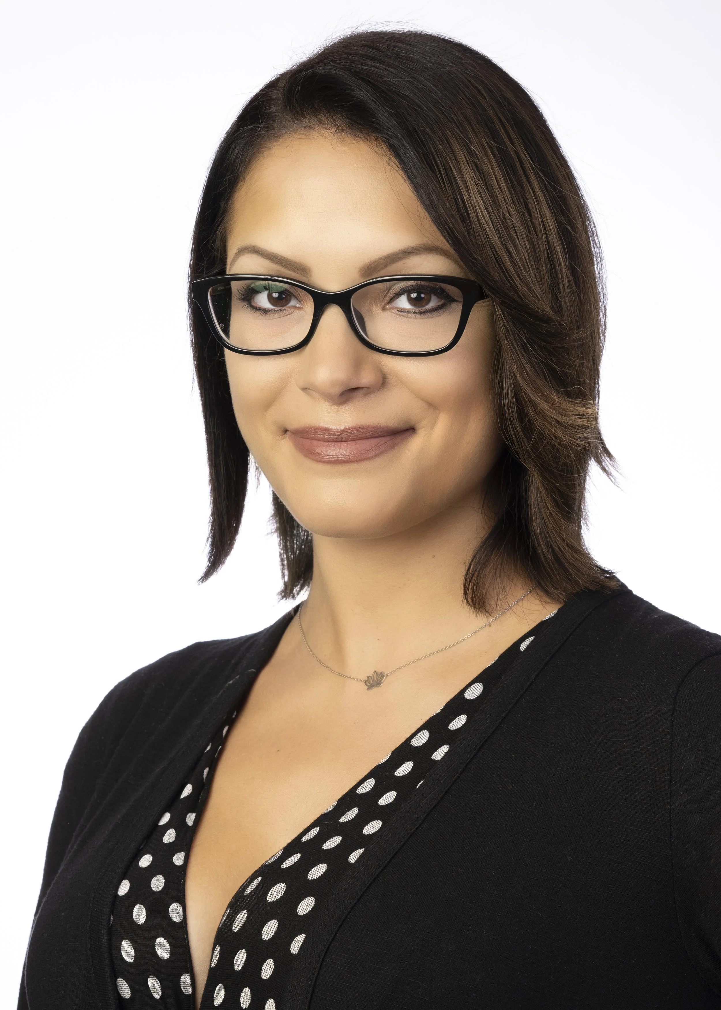This photo is of a woman on a flat white background taken on location. The headshot photographer came to the law firm's office to take staff photos as well. This executive is a woman with brown hair and dark rimmed glasses.