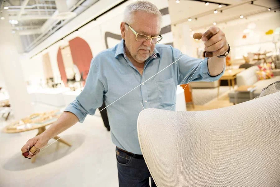 An older man with glasses and a blue shirt adjusting a lamp in a furniture store.