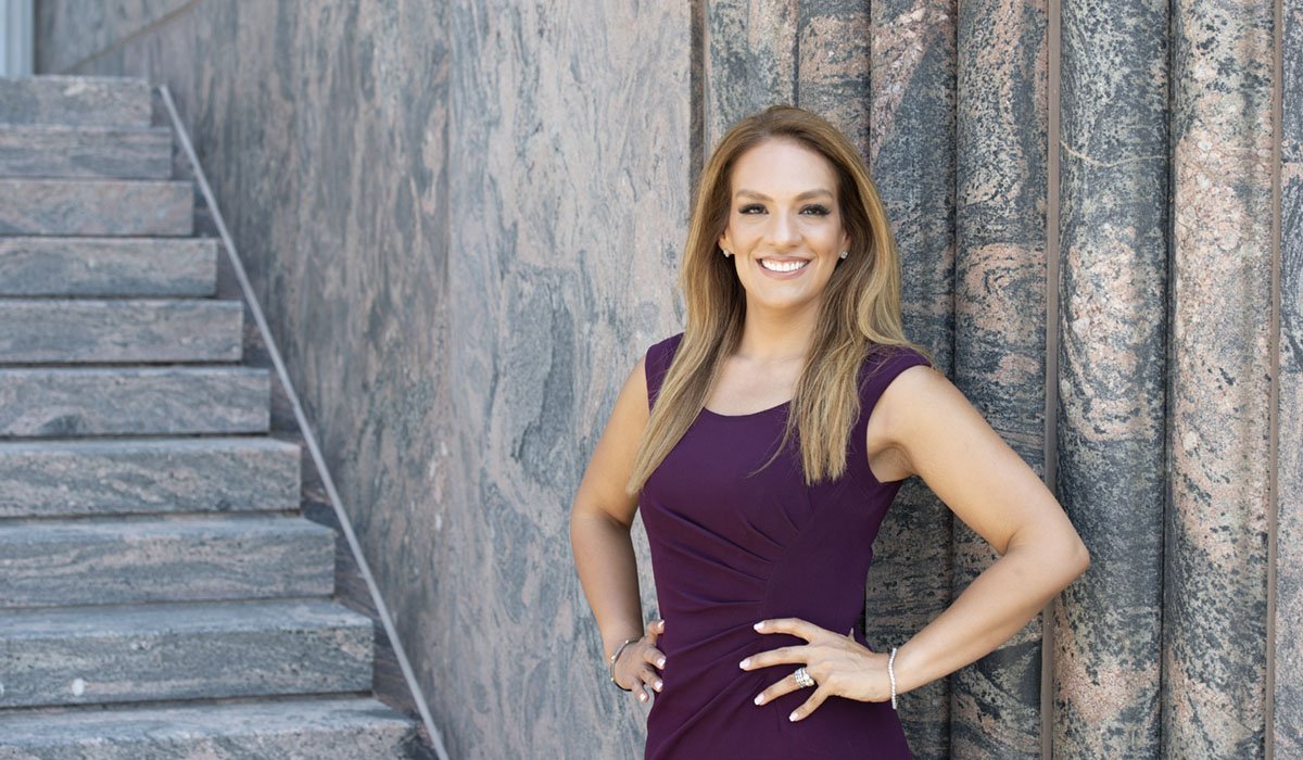 A Chicago photographer captures a portrait of a luxury real estate agent. The realtor has an upscale brand in Lincoln Park and the marble behind her shows that off. She is wearing a purple dress and has her hands on her hips.