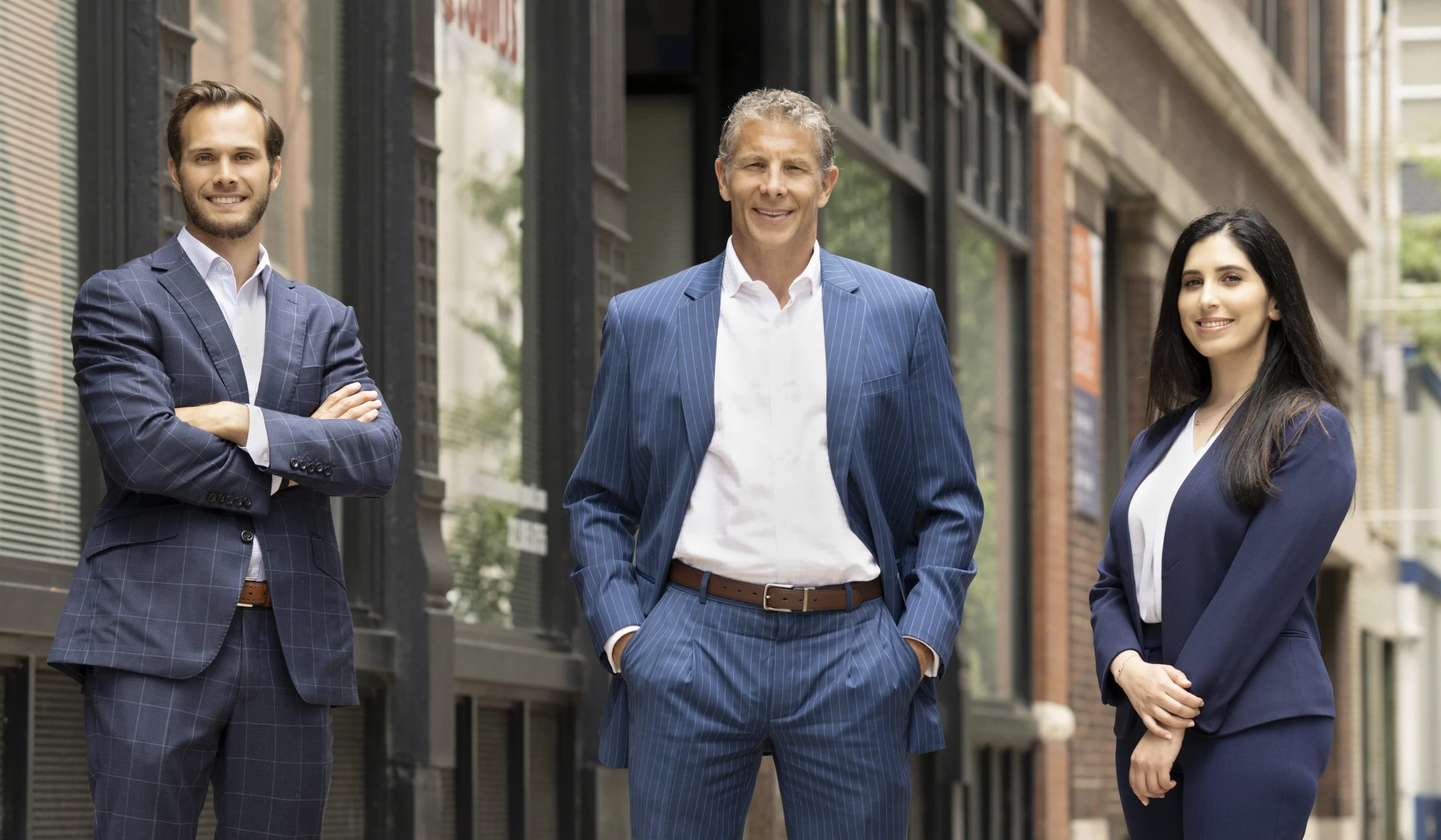 Three professionally dressed individuals standing outside, smiling at the camera.