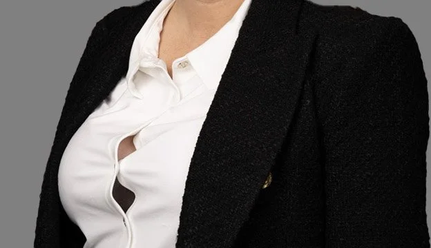 Close-up of a woman wearing a black blazer over a white button-up shirt with a small notch.