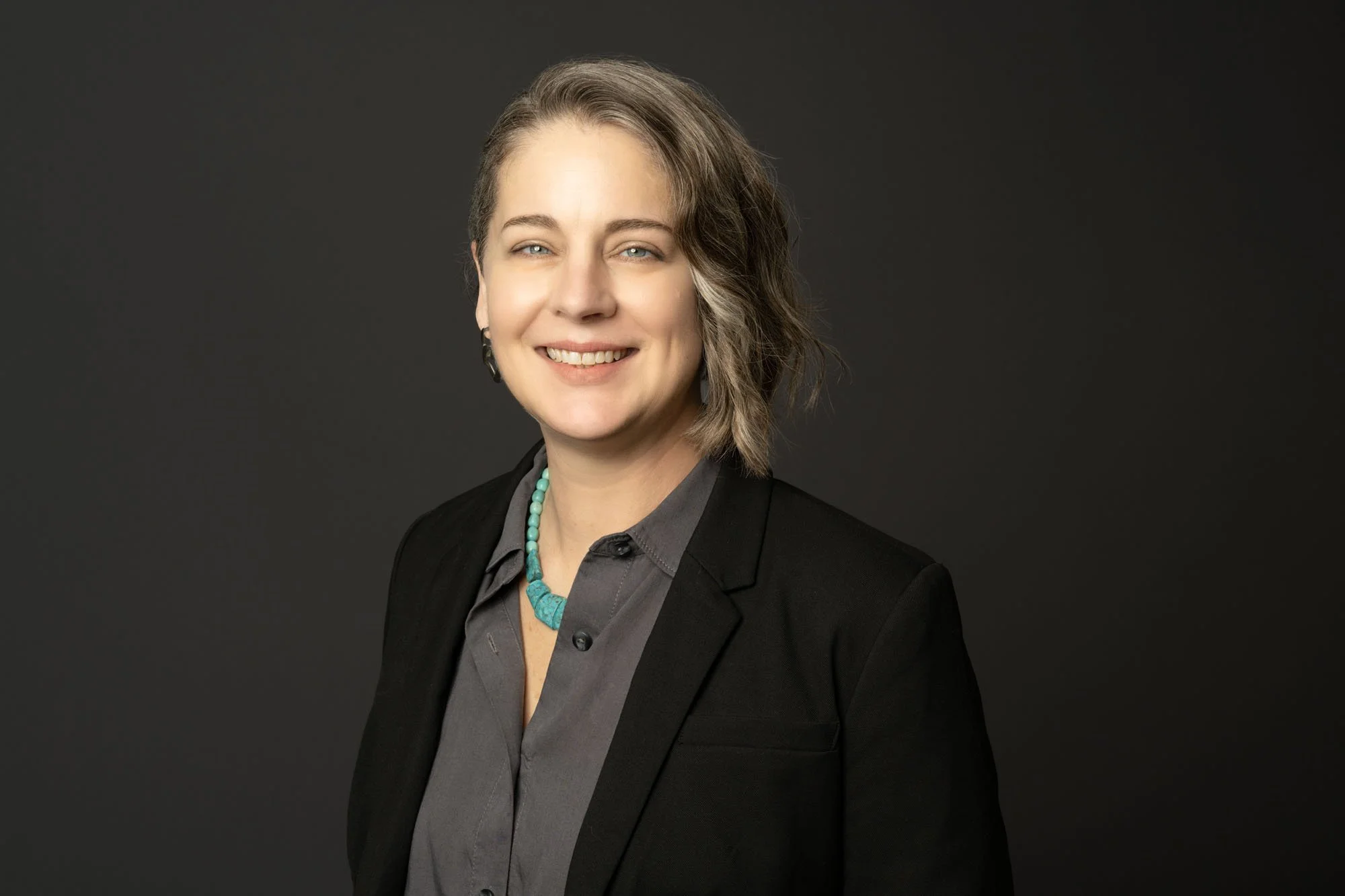 Horizontal professional headshot in Chicago. A woman attorney is on a dark grey solid portable backdrop taken by a top photographer.