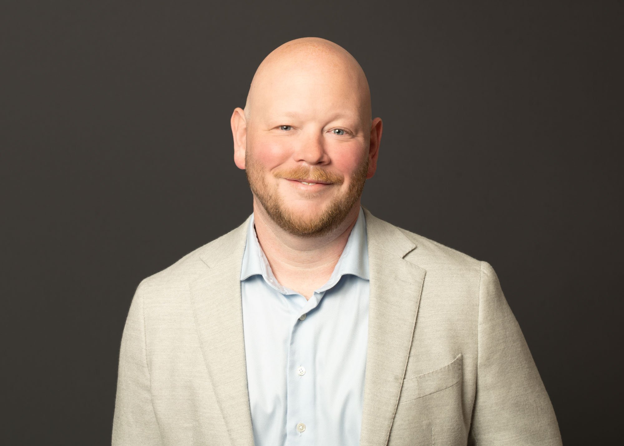 A man in a sport coat and dark backdrop taken on location. This was taken with a portable studio at their downtown office of their entire staff and while photographing all of their employees for consistency. All off the Chicago staff headshot photogr
