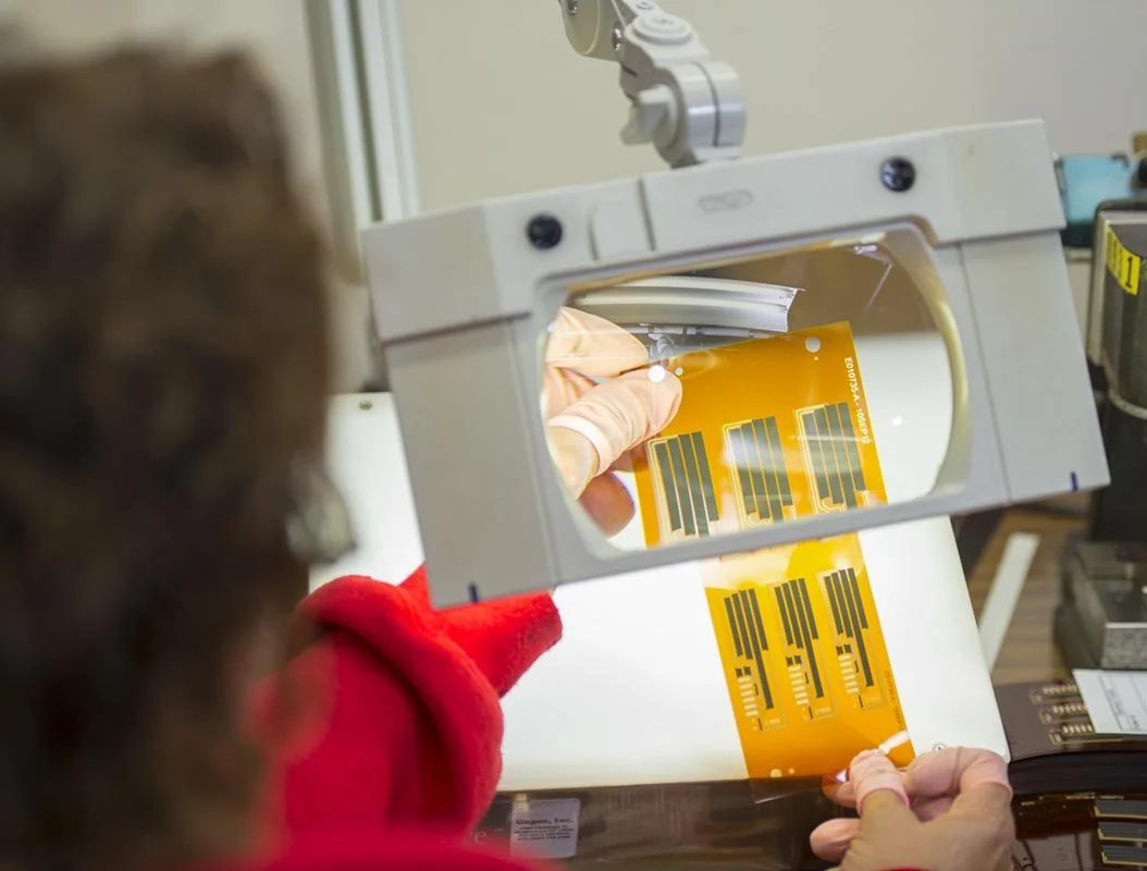 Person holding a microchip behind a transparent shield with information labels, viewed from behind.