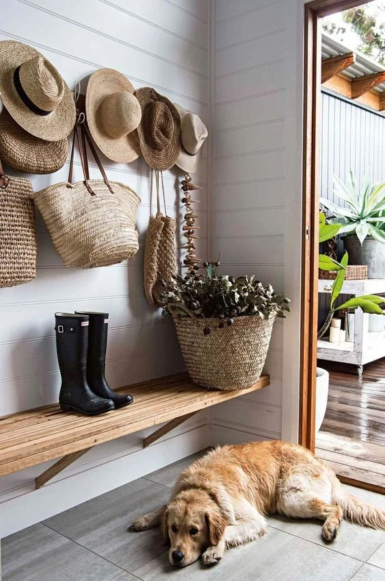 A rack holding sun hats and straw bags as wall decor above a bench in an entry hallway