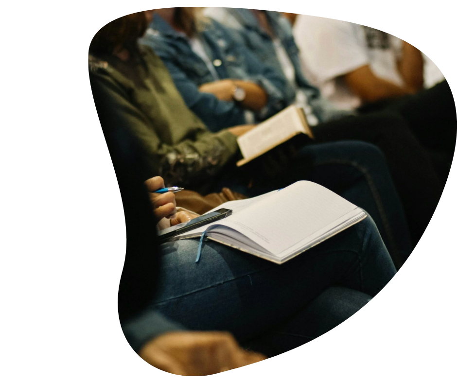 People seated in a row, holding notebooks and pens, possibly attending a class or seminar.