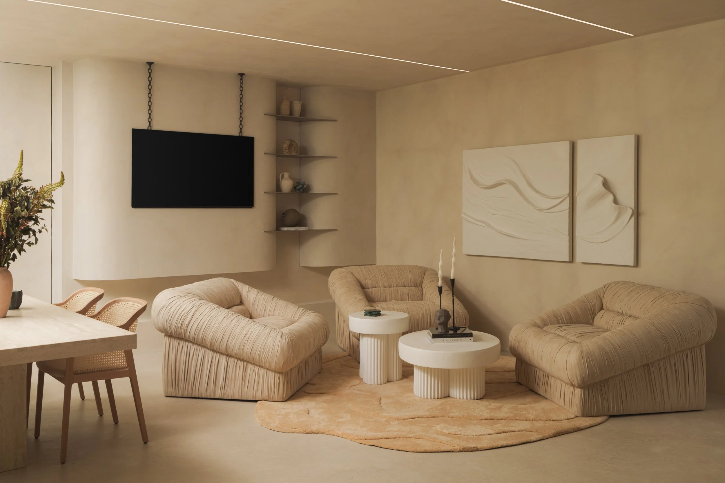 Modern living room painted in Bauwerk limewash BONE with beige plush armchairs, round white coffee tables, abstract wall art, a mounted flat-screen TV, and decorative items on shelves. Light-colored walls and a beige rug.