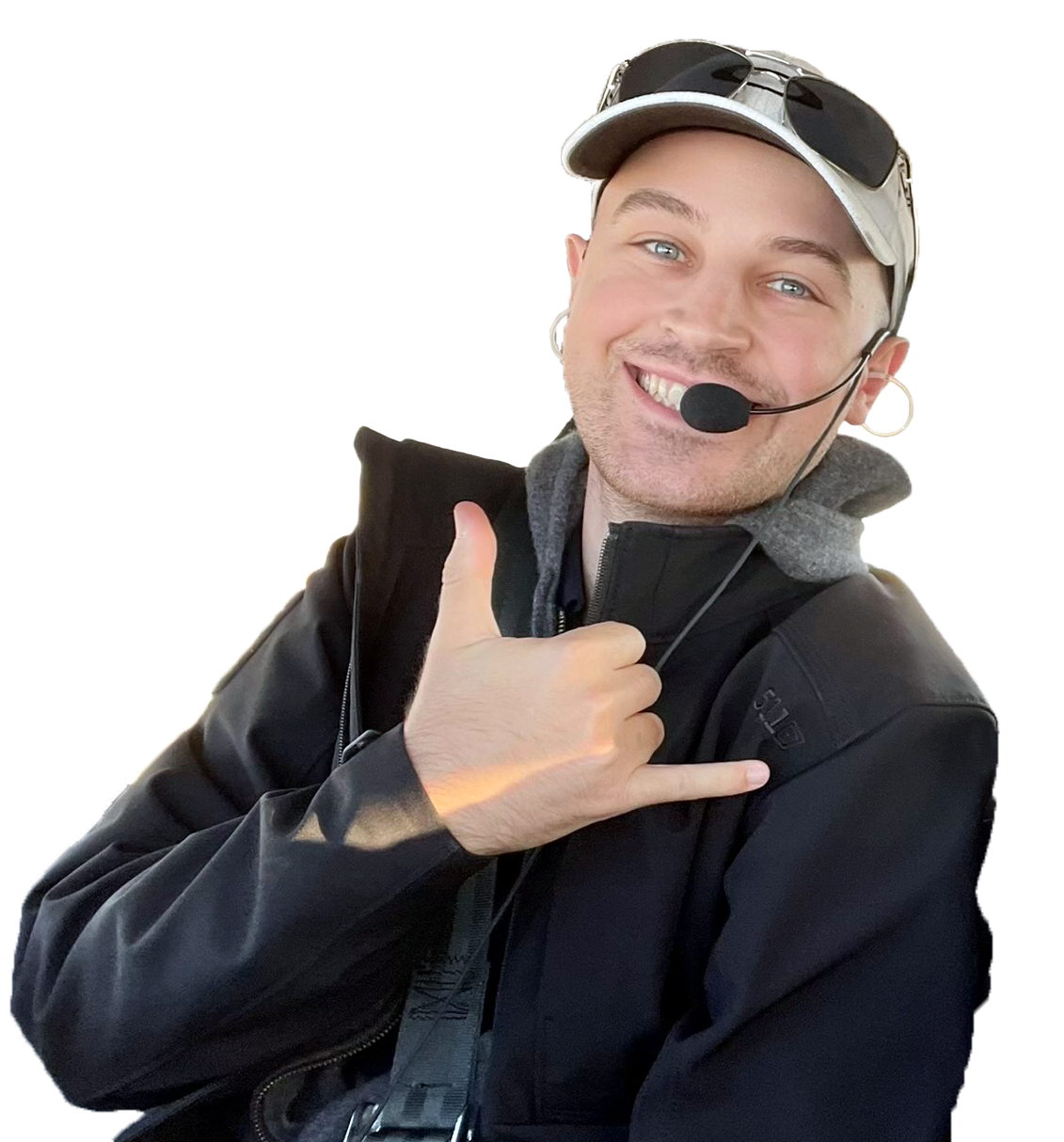 Young man wearing a headset with a microphone, a cap, sunglasses on his head, making a thumbs-up gesture and smiling.