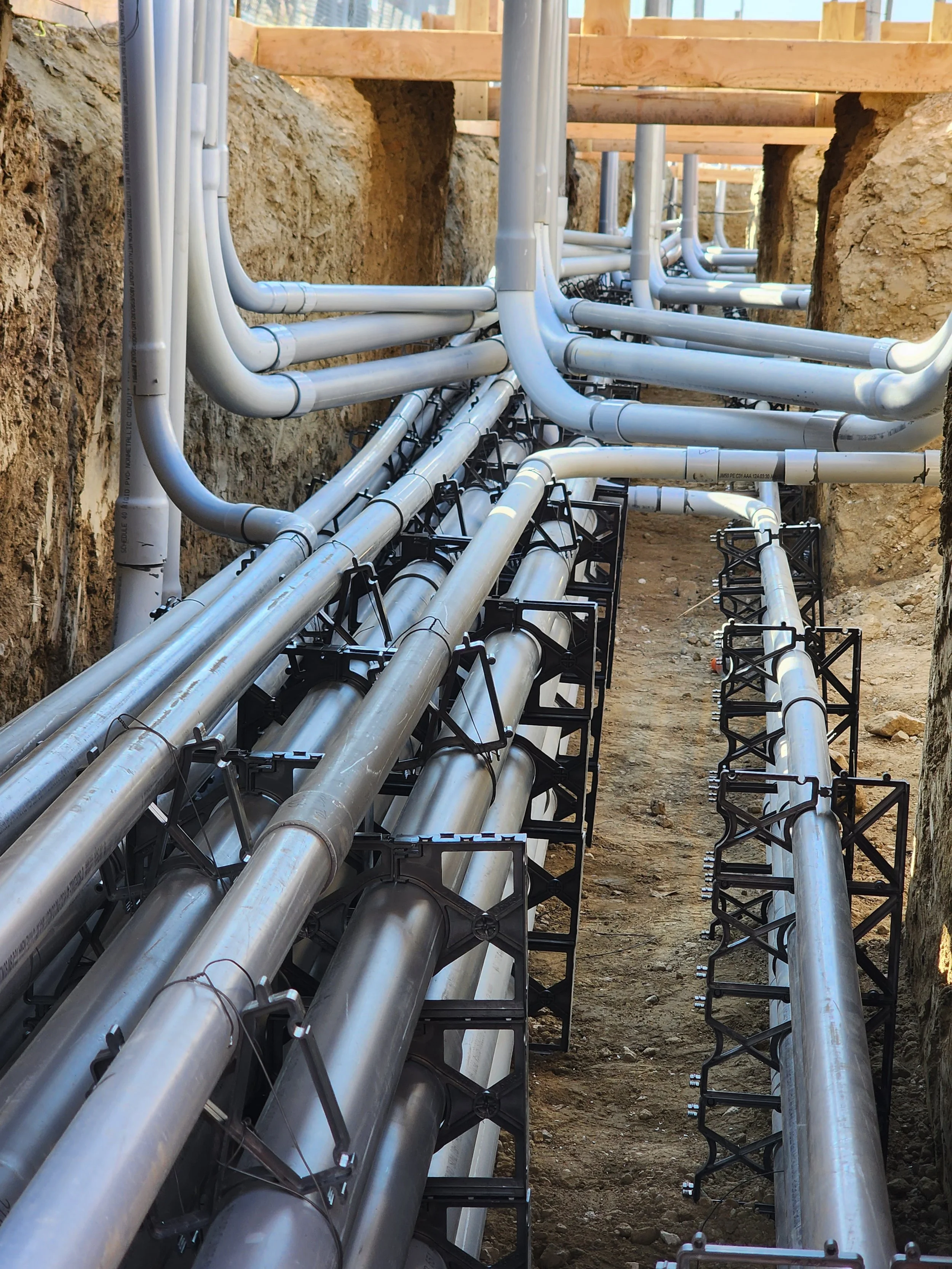 Underground electrical conduit installation in a trench for high-power port EV charging infrastructure, featuring complex PVC pipe routing and spacers.