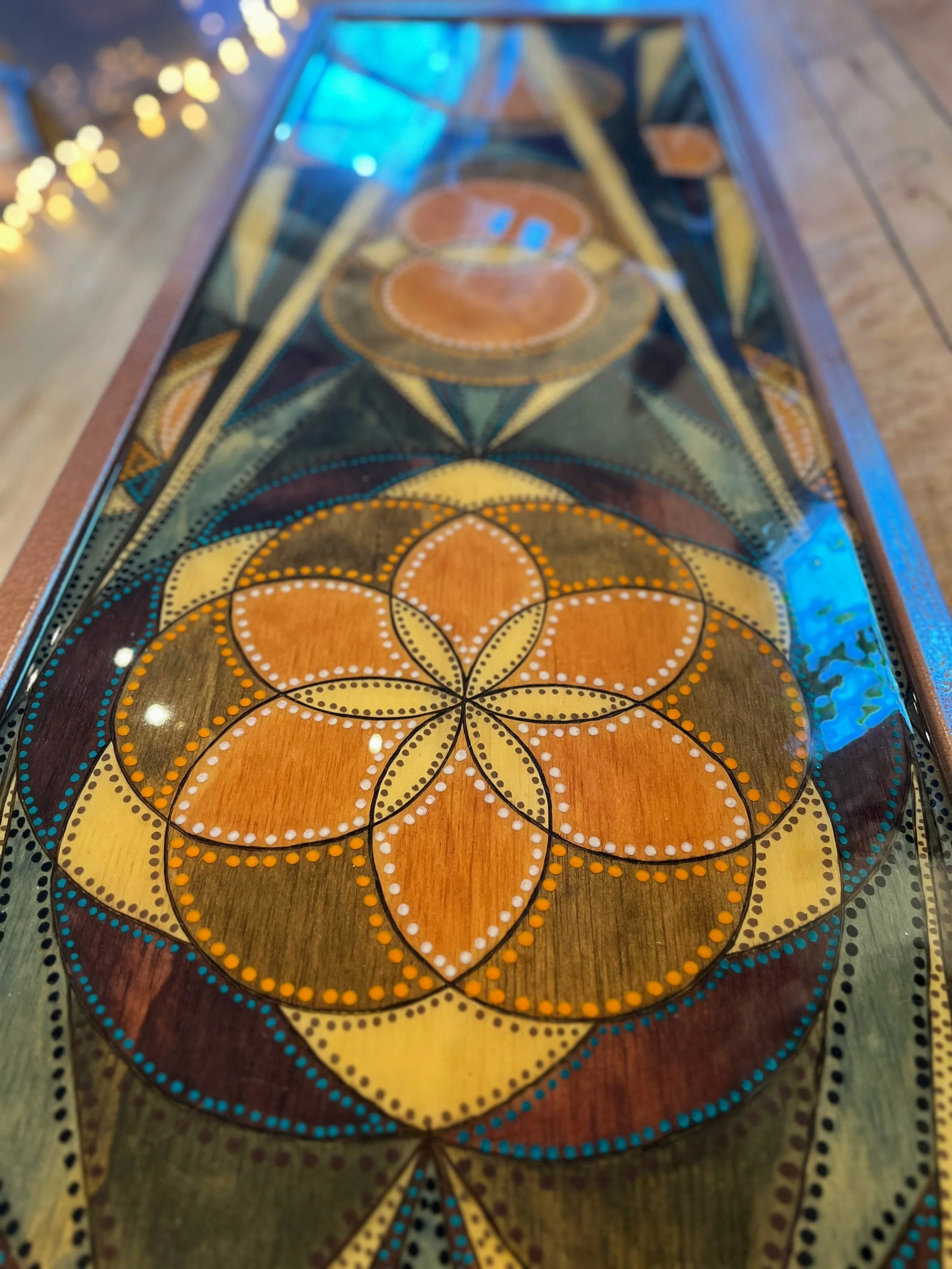 Close-up of a detailed geometric art design featuring overlapping circles and petal shapes with multicolored dots on a glossy surface.