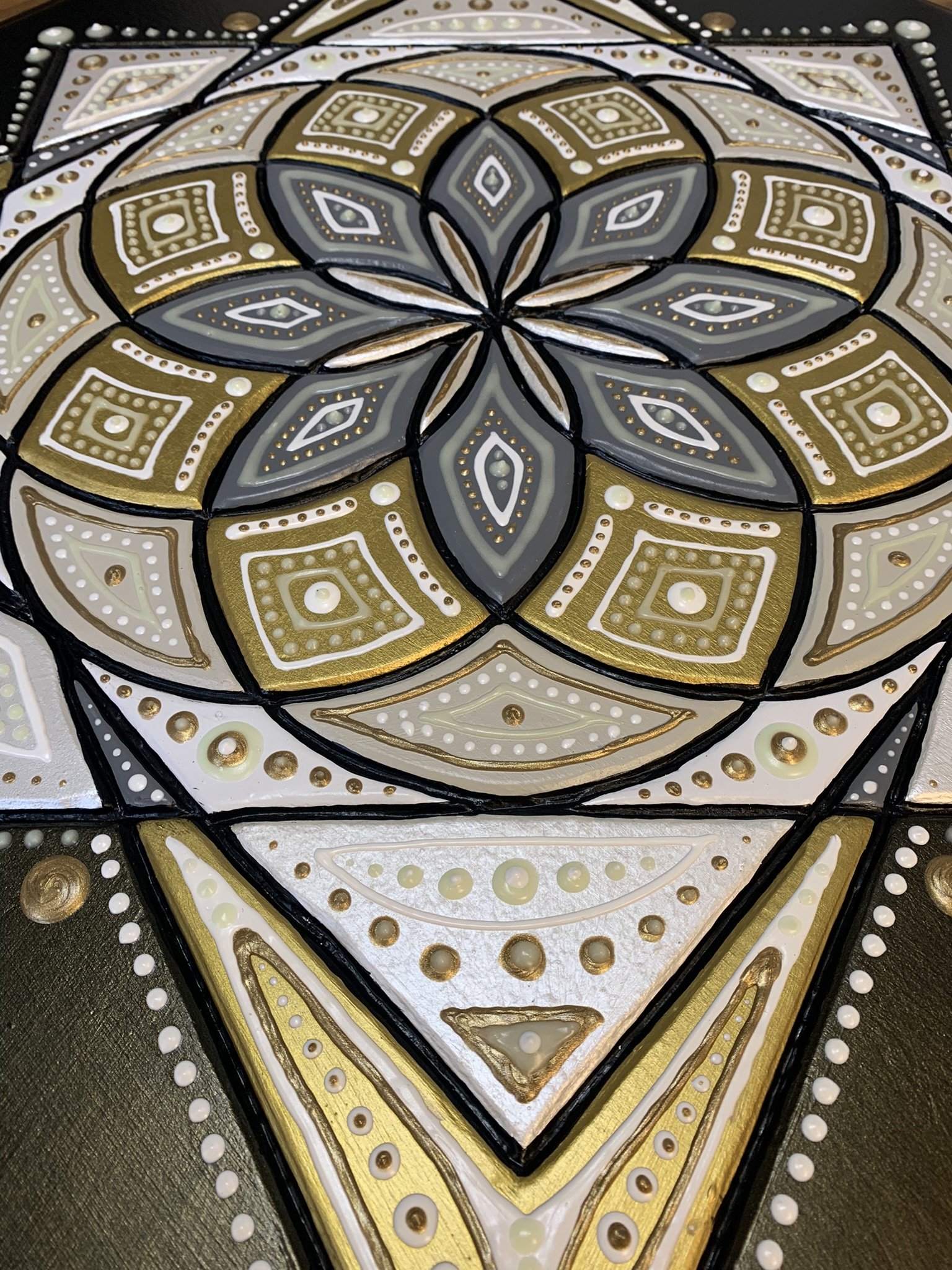 Intricate mandala pattern in black, white, gold, and gray colors with geometric shapes and dots.