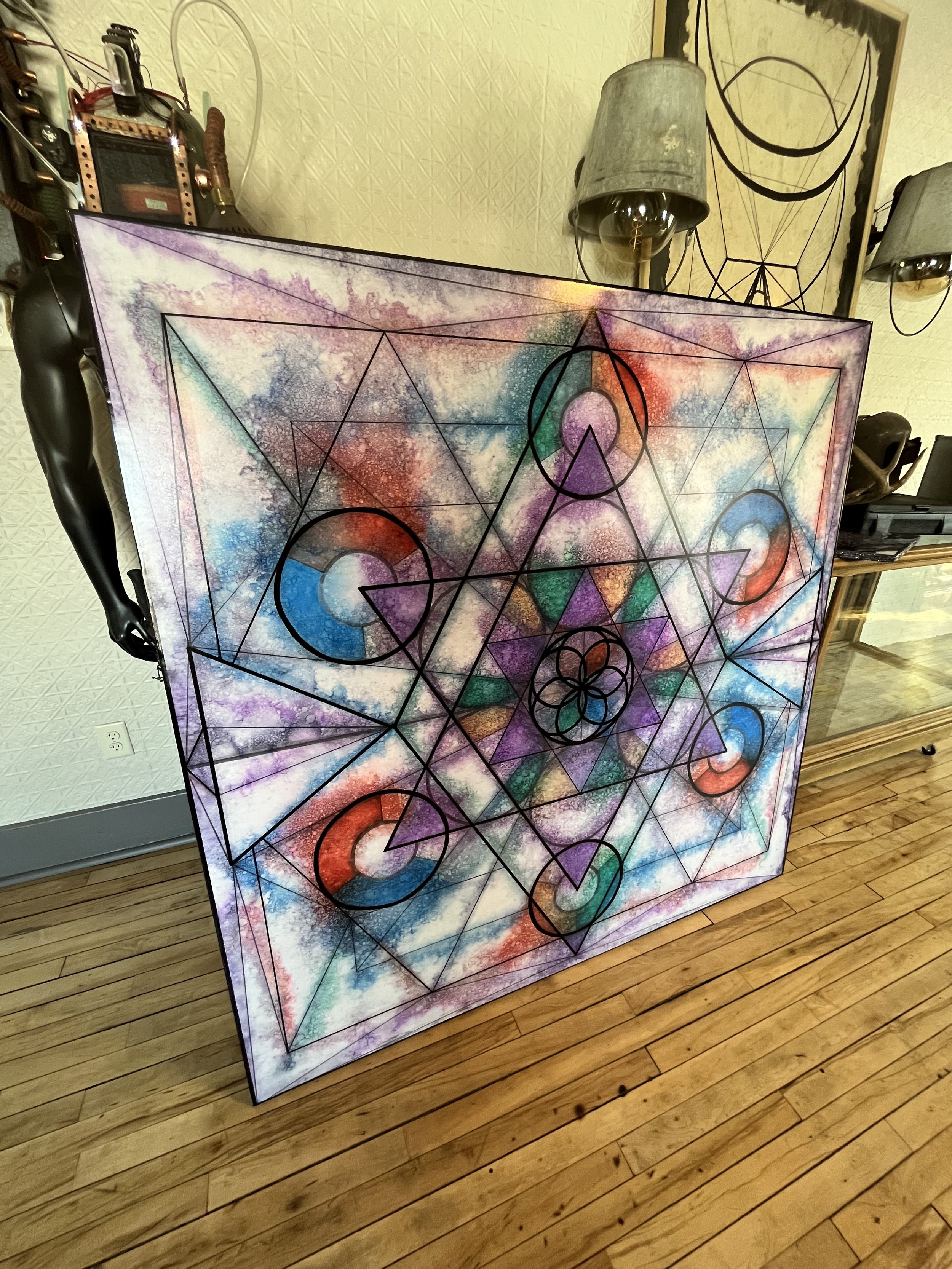 Colorful geometric abstract artwork leaning against a wall, featuring a combination of circles, triangles, and lines in a cosmic color palette.