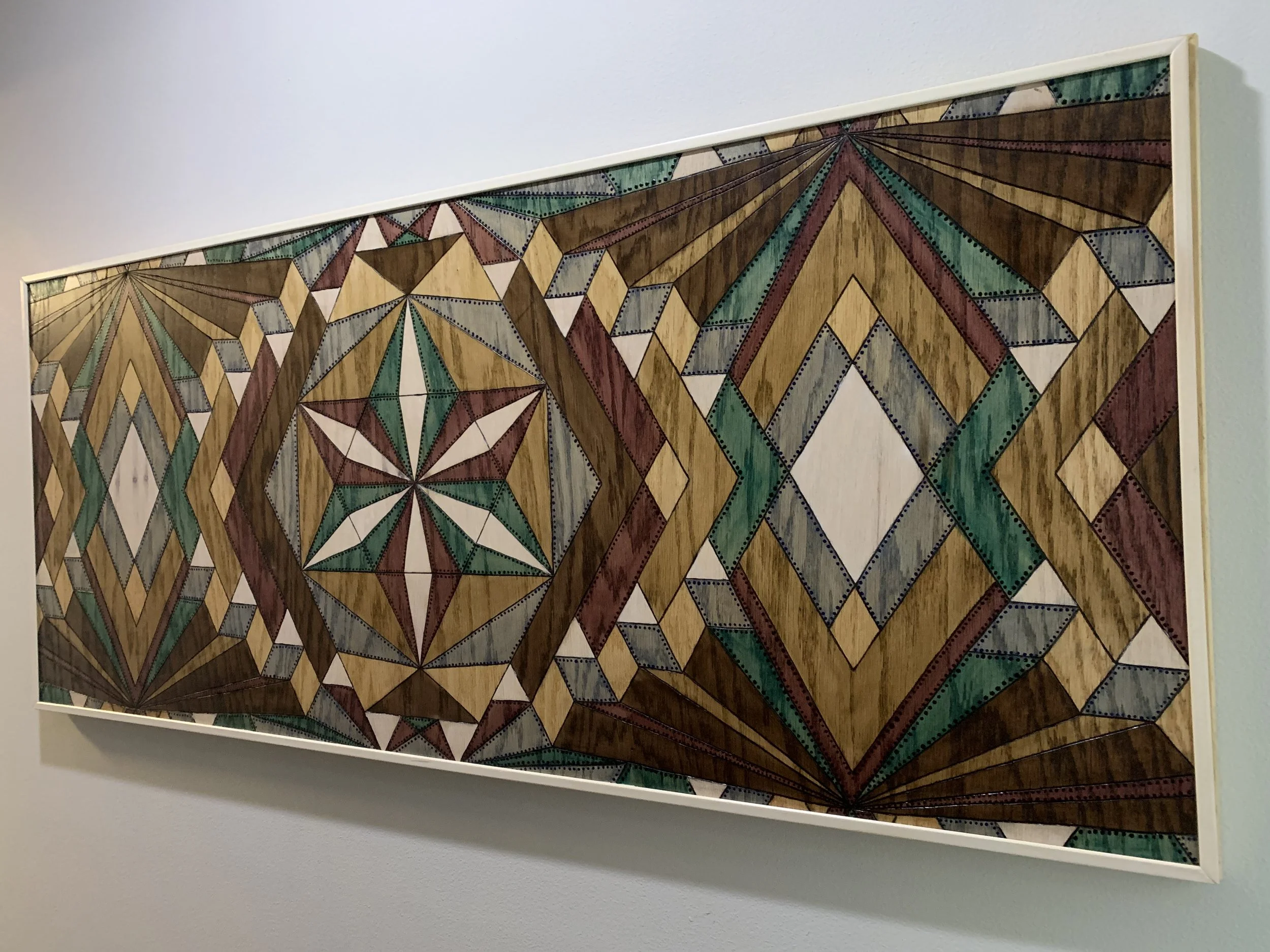 Geometric abstract artwork with diamond and star patterns in earthy tones framed on a wall.