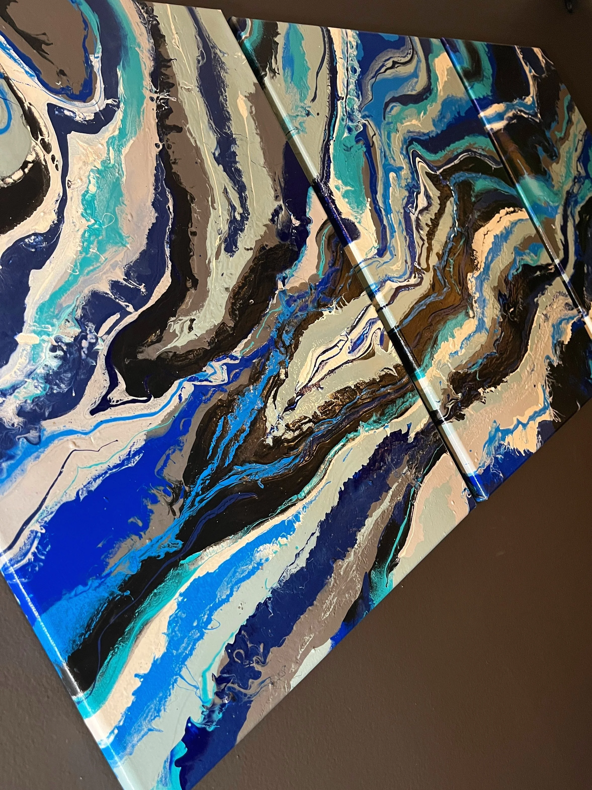 Abstract painting with swirling blue, black, beige, and white patterns on three connected canvases.