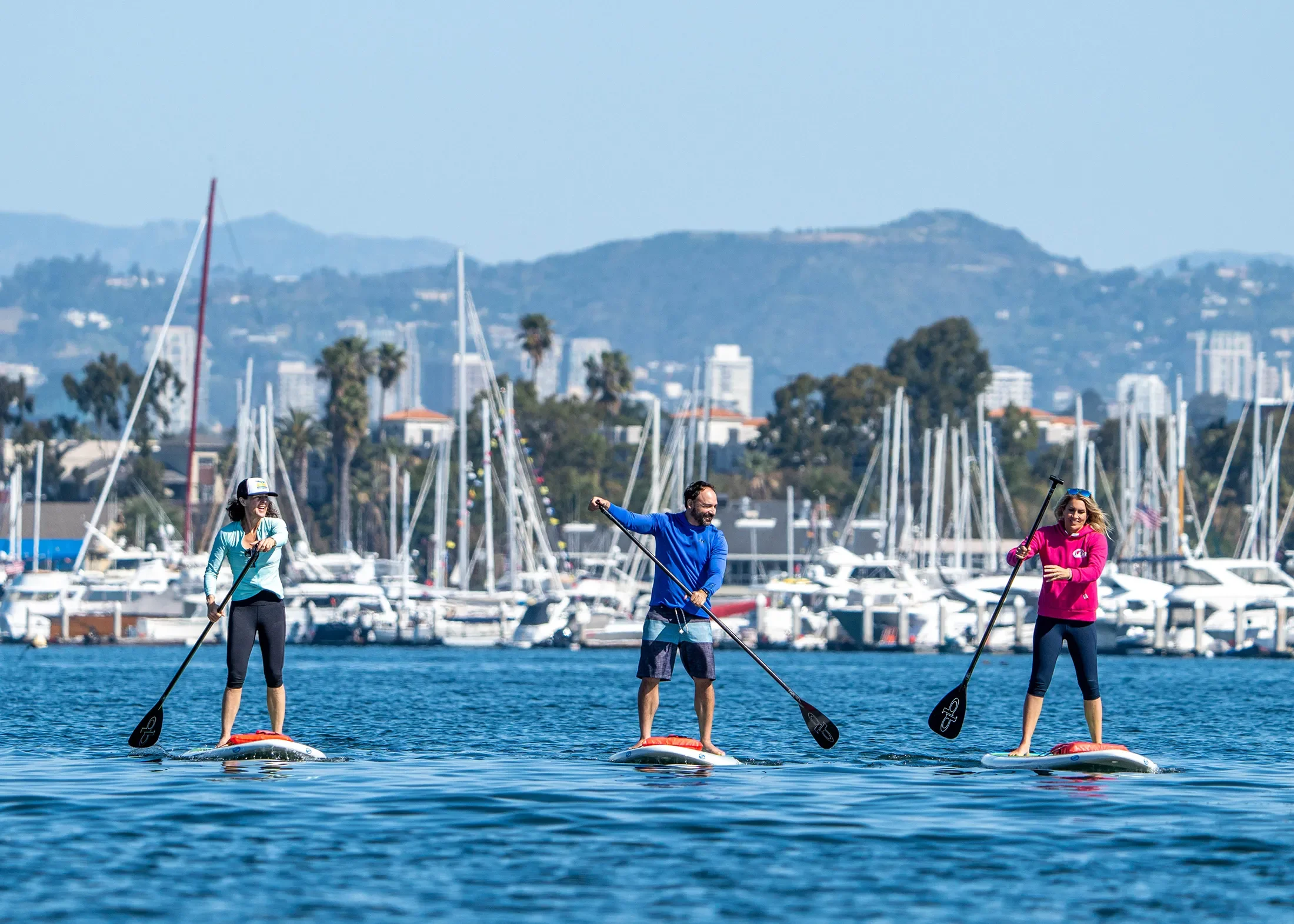 incredible view of los angeles hills from marina del rey with paddleboarders on pro sup shop rental boards and sailboats on docks