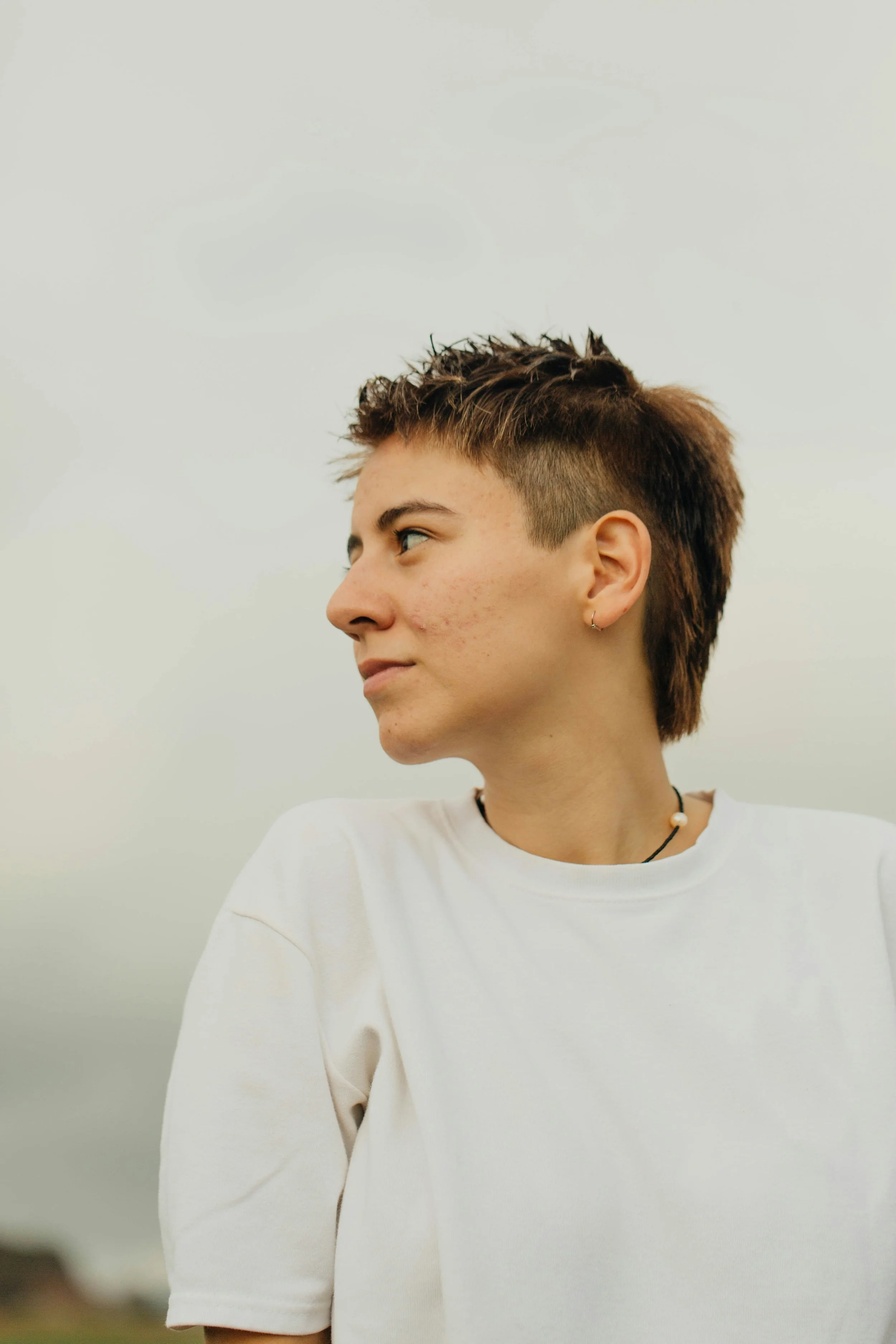 A person with short hair and a white shirt looks off to their right