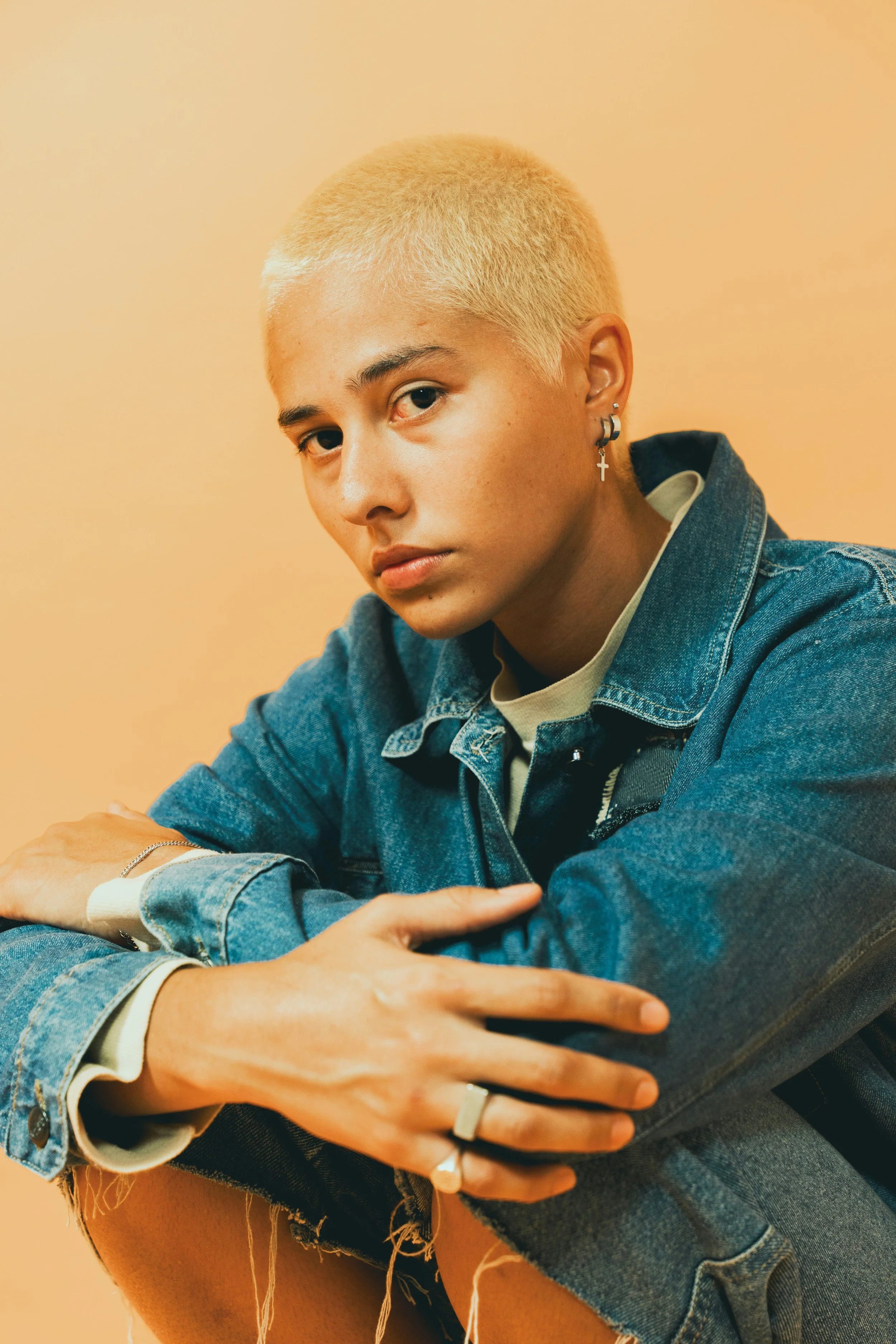 A person with shaved, bleached hair hugs themselves