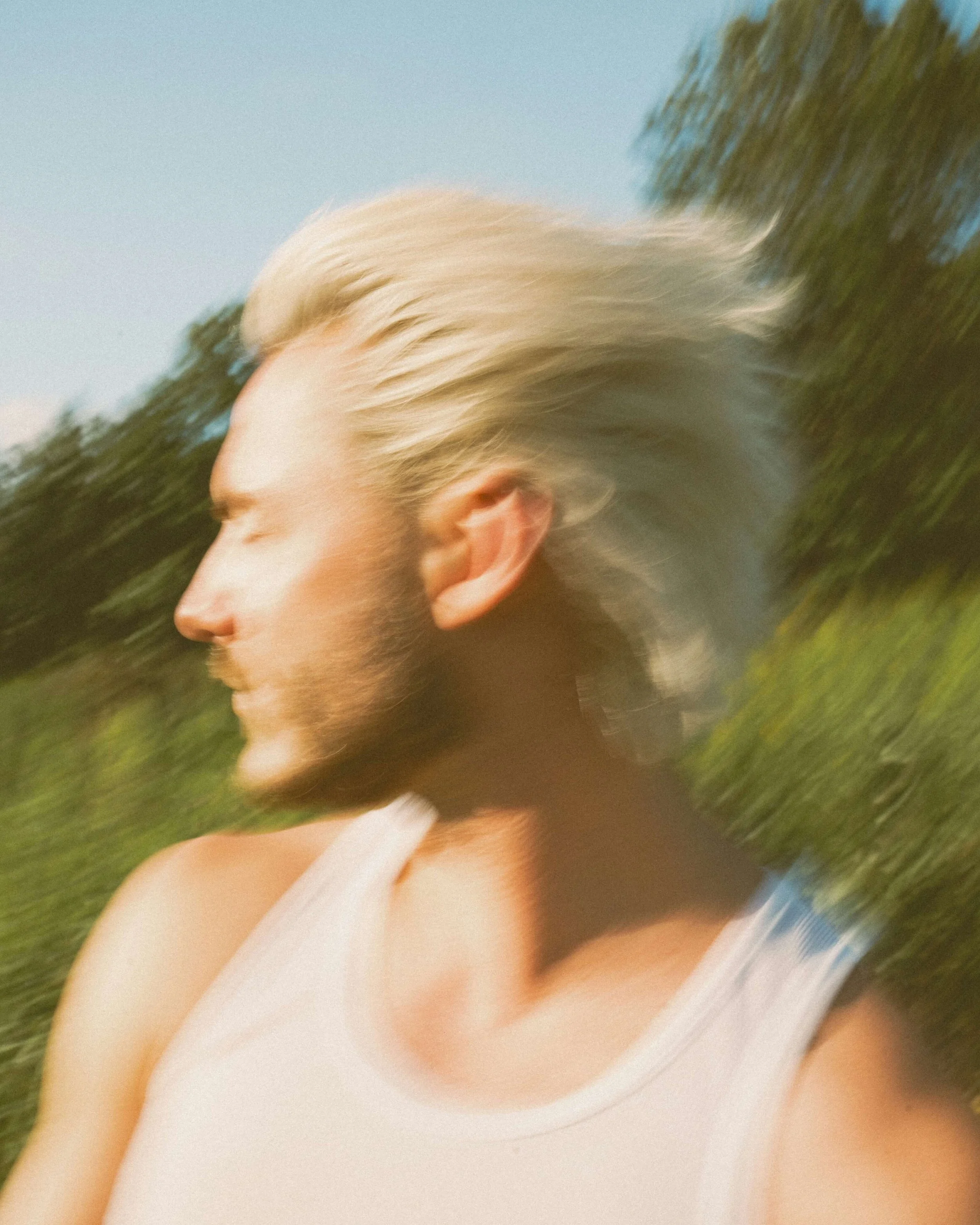 Blurred motion photo of a person's profile, standing outside in a white tank top
