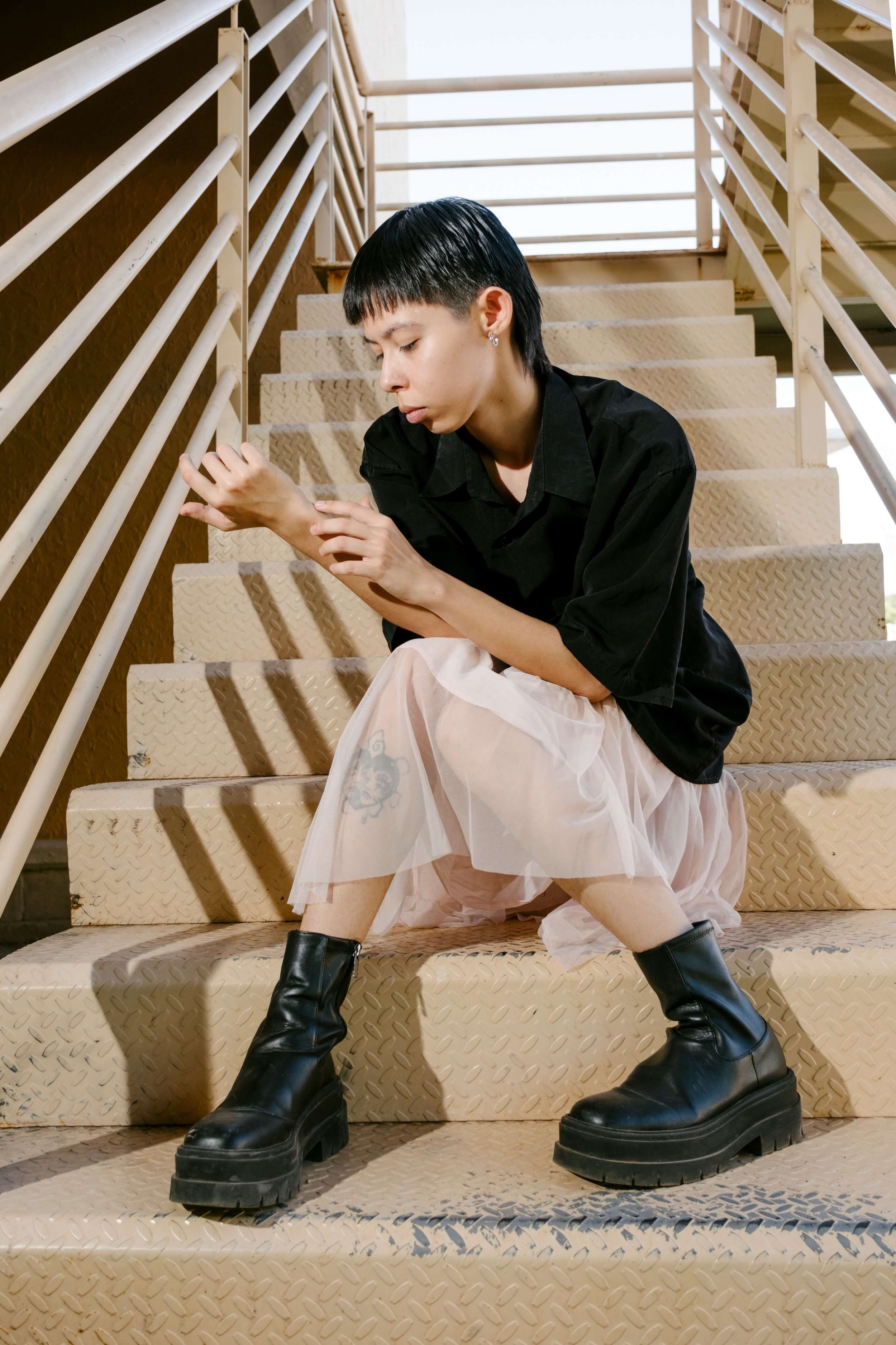 A person who short black hair sits on the stairs, looking down at their hands - somatic therapy st paul