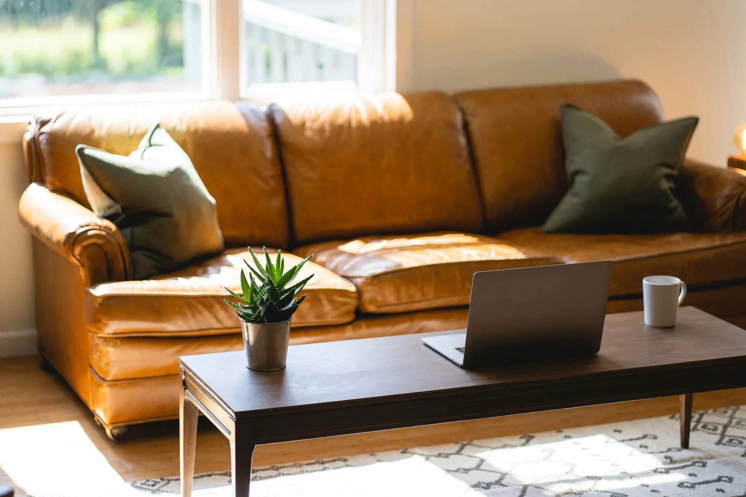 An office with a brown leather sofa and sunlight pouring in