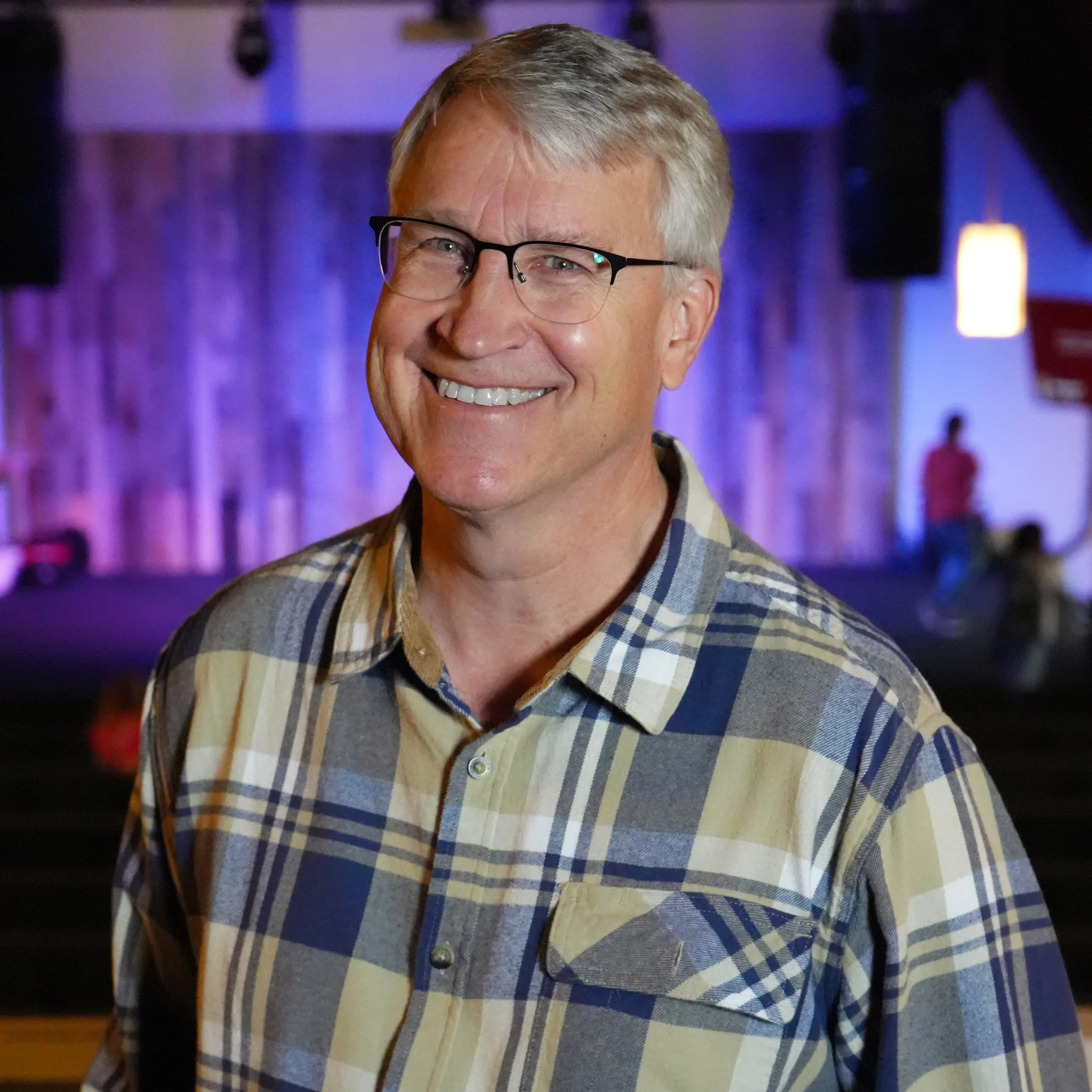 Smiling person with glasses in a crowd on a cobblestone street.
