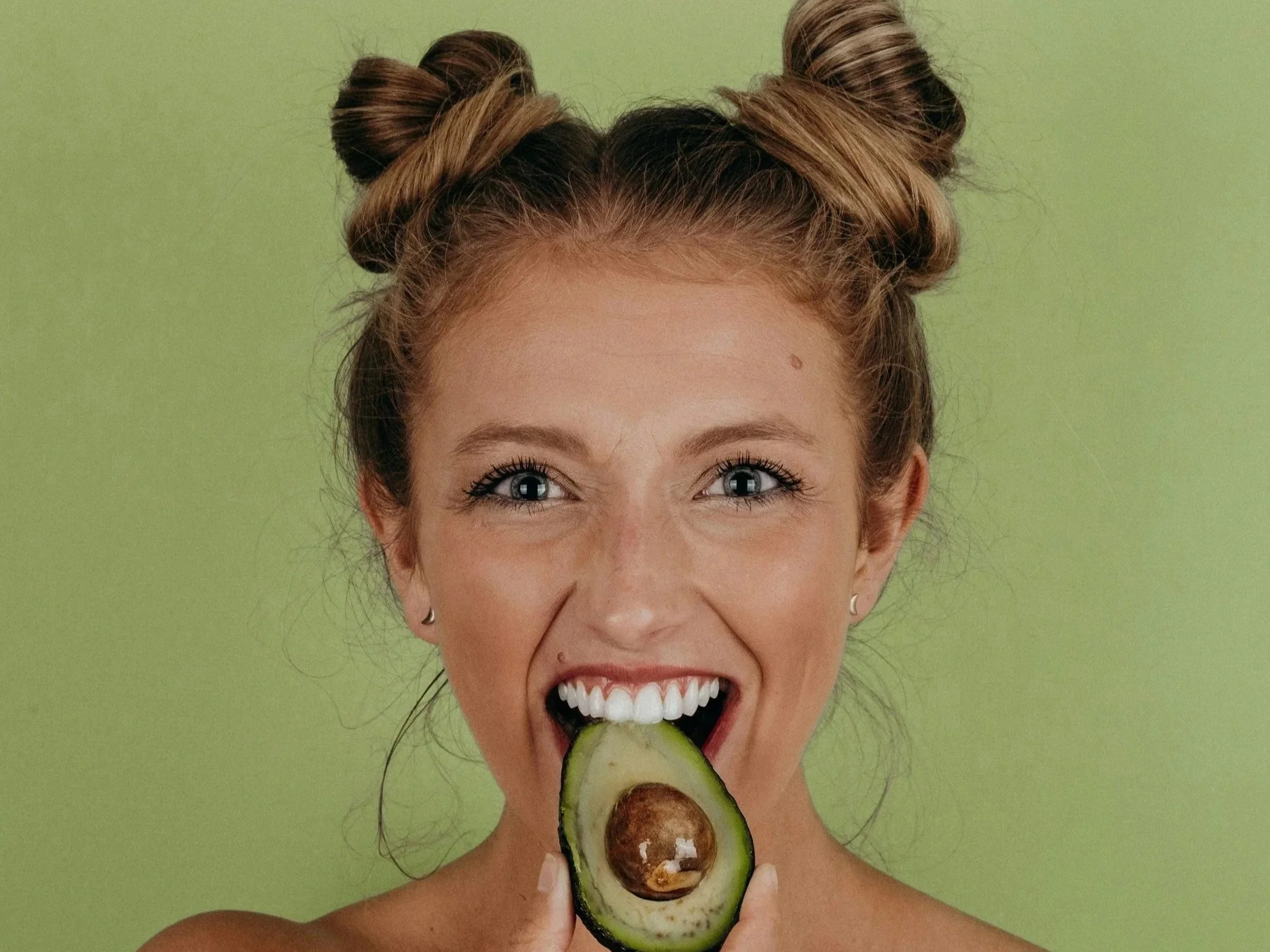 Happy woman holding an avocado, enjoying high-fibre foods that support digestion, reduce bloating, and promote gut health.