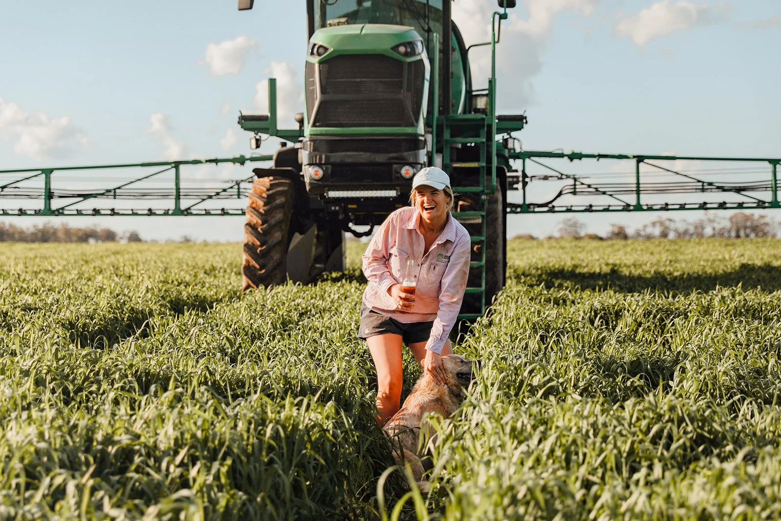 Heidi in a field with a beer in hand in front of farm machinery