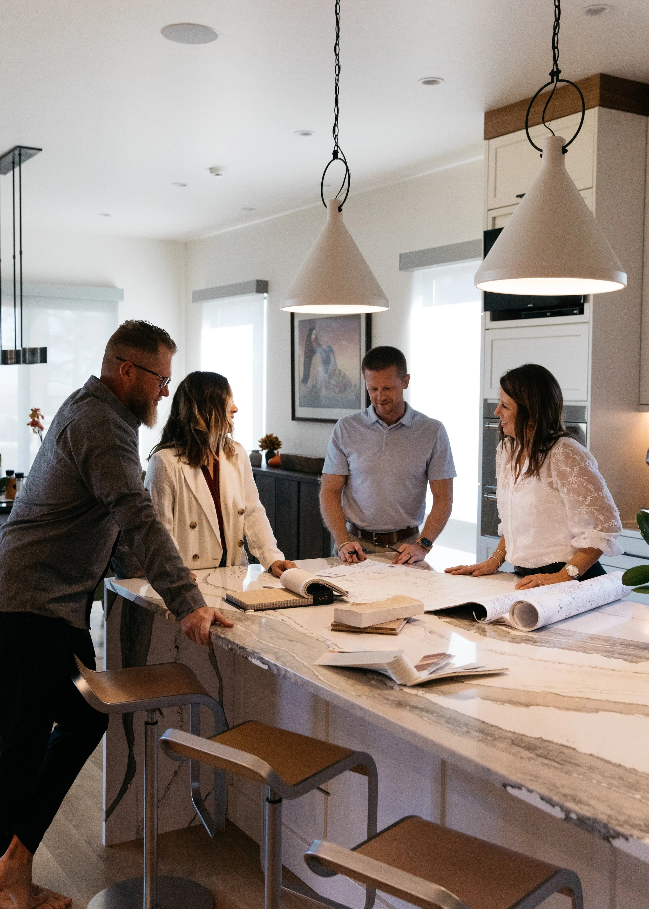 Group of five people discussing plans at a kitchen island with blueprints and samples in a modern home.