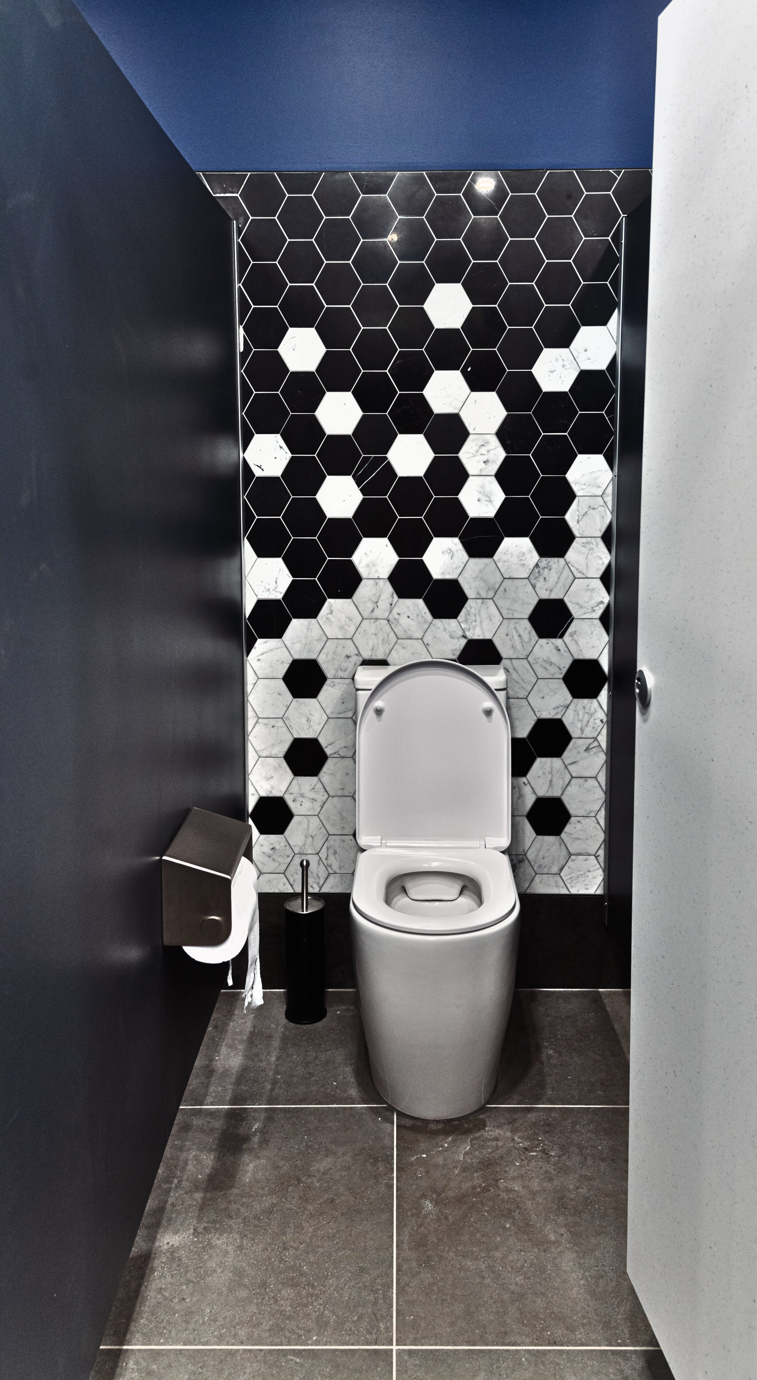 A modern bathroom with black and white hexagonal tiled wall, a white toilet, and dark gray floor tiles.