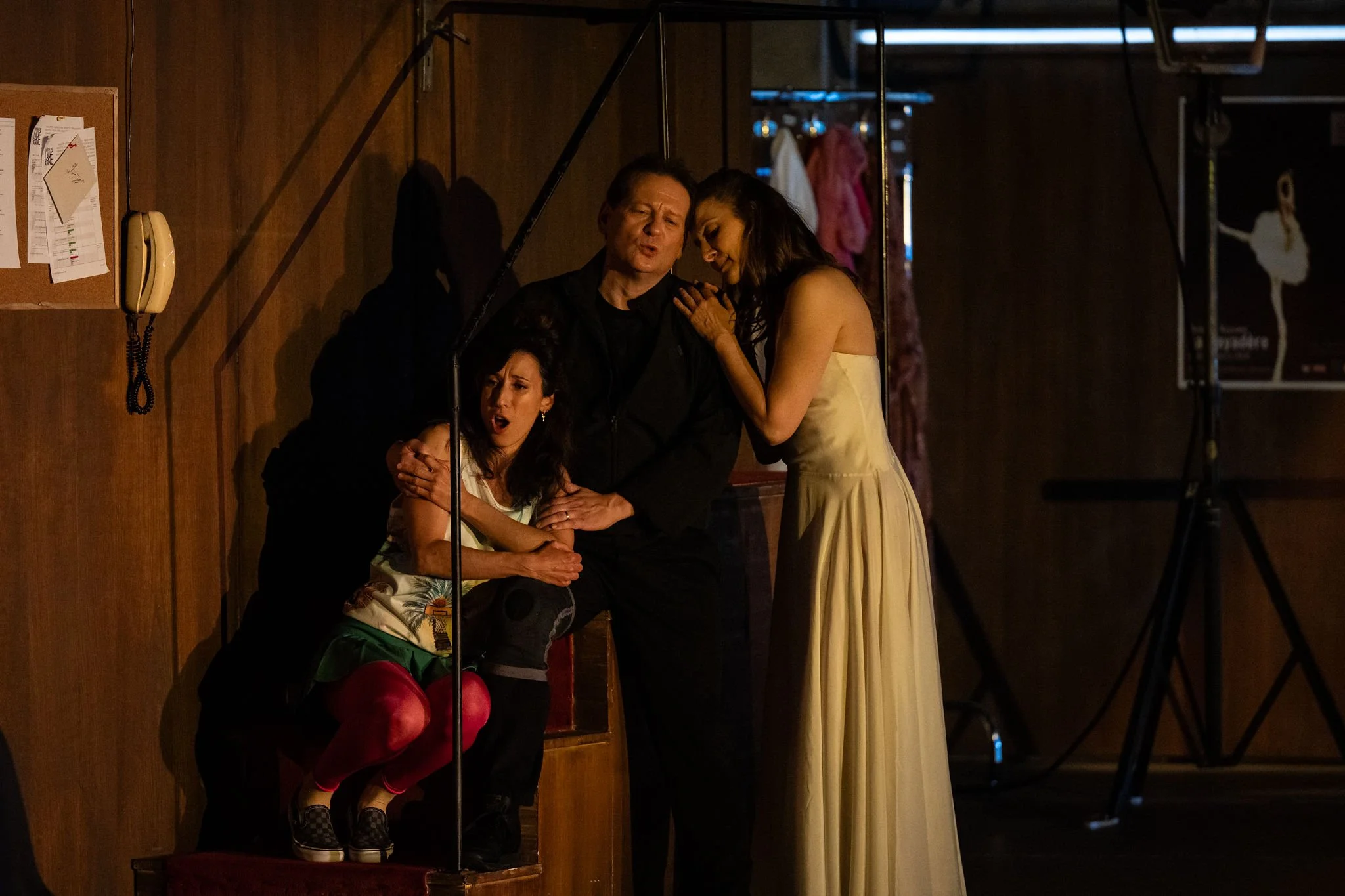 Three actors on stage during a theatrical performance. The man in the center appears to be singing or speaking passionately, with two women on either side showing expressions of emotion and engagement.