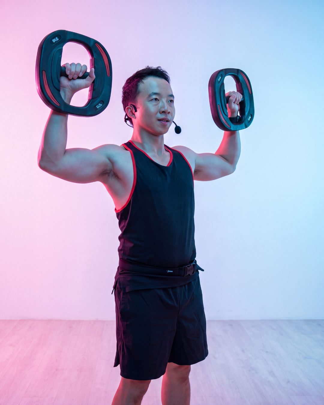 Dennis F, TeamX BODYPUMP® instructor in Hong Kong, holding weight plates overhead during a strength class.