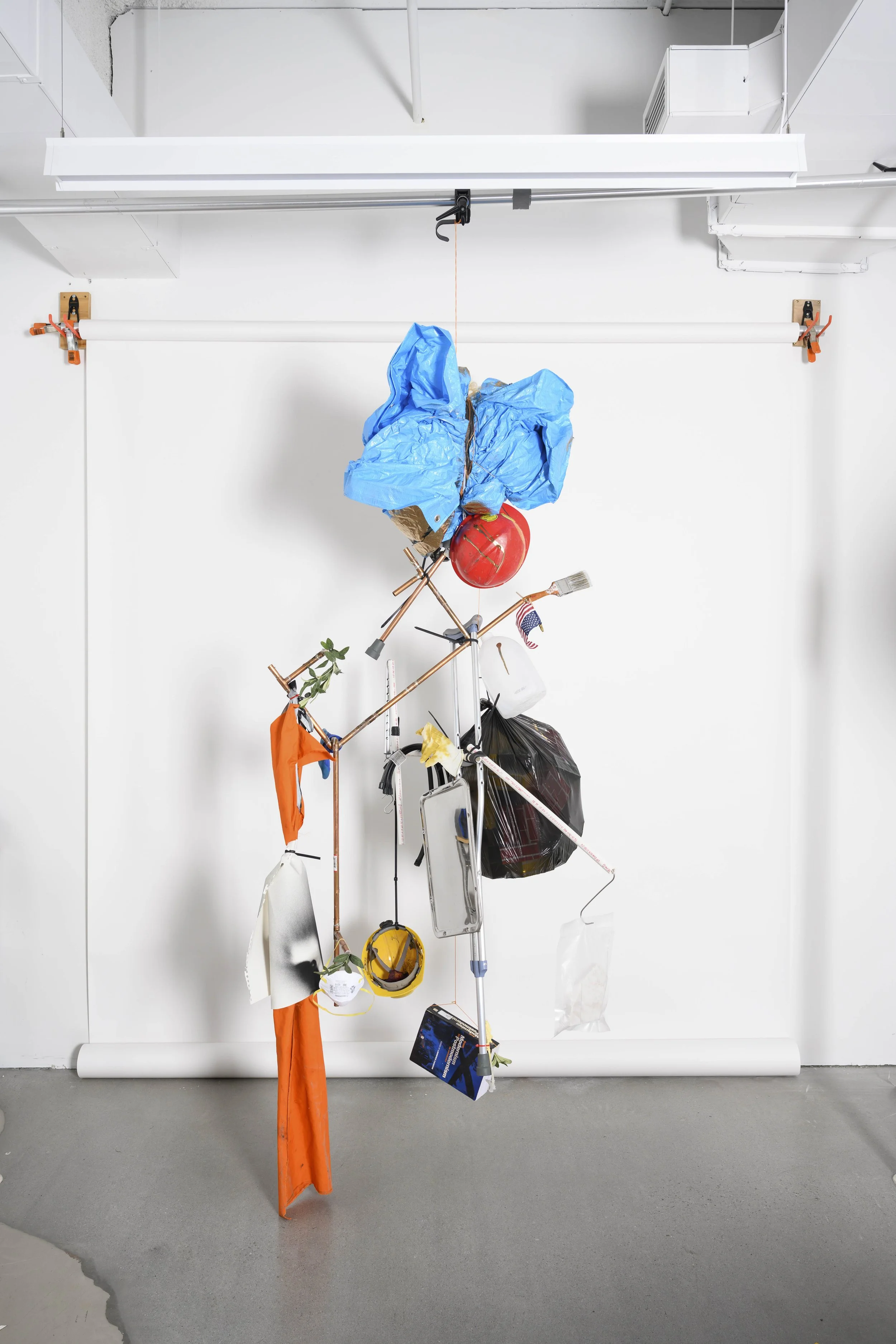 In(tension), 2026 (120 x 48 x 52”) width/depth variable
Nylon string, tarp, construction helmets,
copper tubing, faux olive branches,
tape, crutch, aluminum can, nylon
fabric, safety mirror, dust mask, PVC,
latex glove, rubber glove, rose petals,
pur