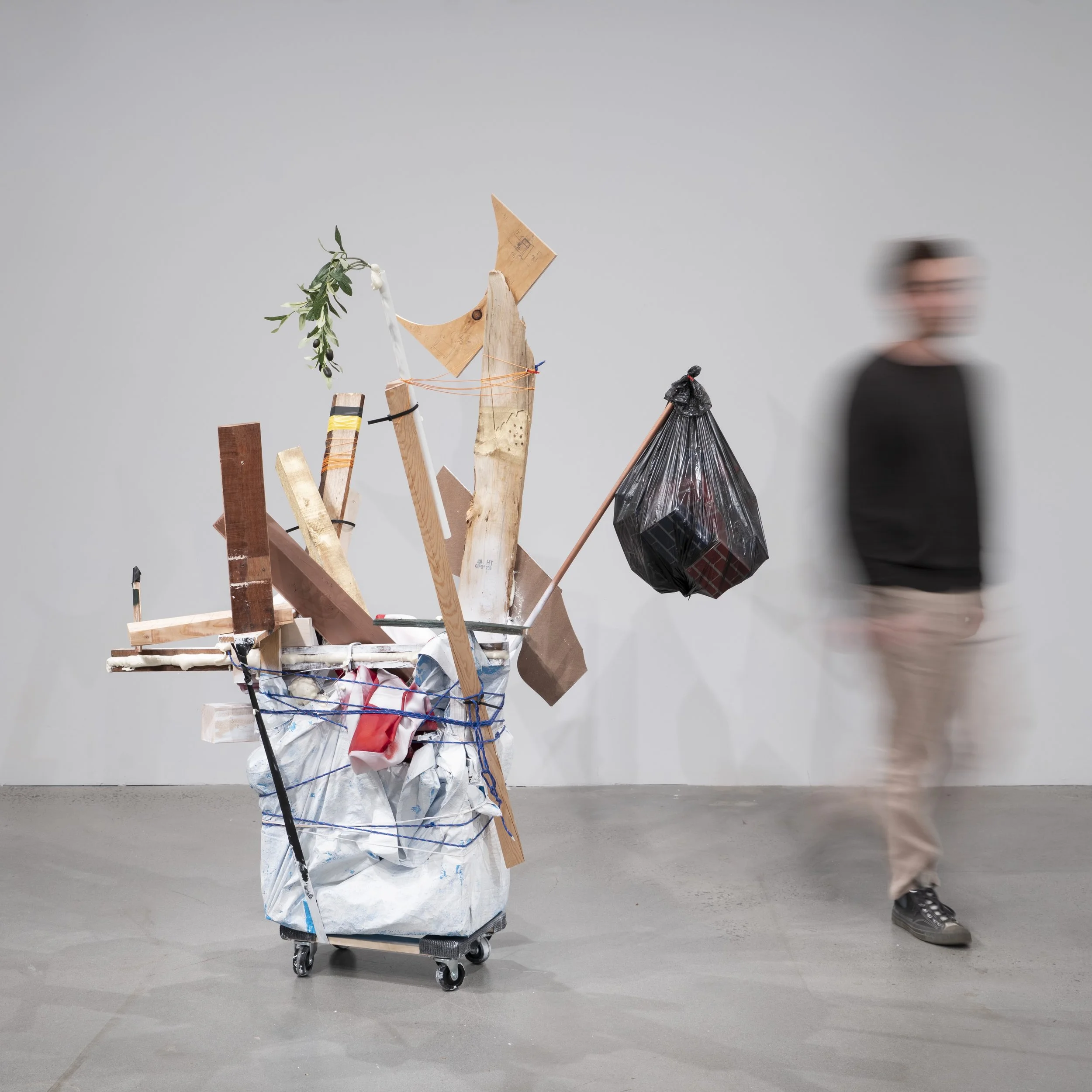 What We Carry, 2026 (73 x 61 x 17") reclaimed lumber, drop cloth, flag, acrylic, aerosol paint, yarn, barbed wire, copper tube, plastic, insulation foam, cardboard, tape, wheels, zip ties, PVC, faux olive branch