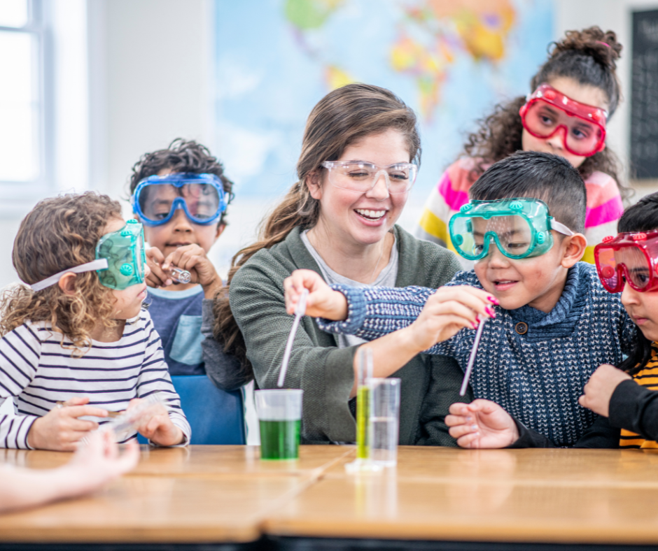 A diverse group of children and their teacher conducting a science experiment in a classroom, with colorful safety goggles and liquids in beakers.