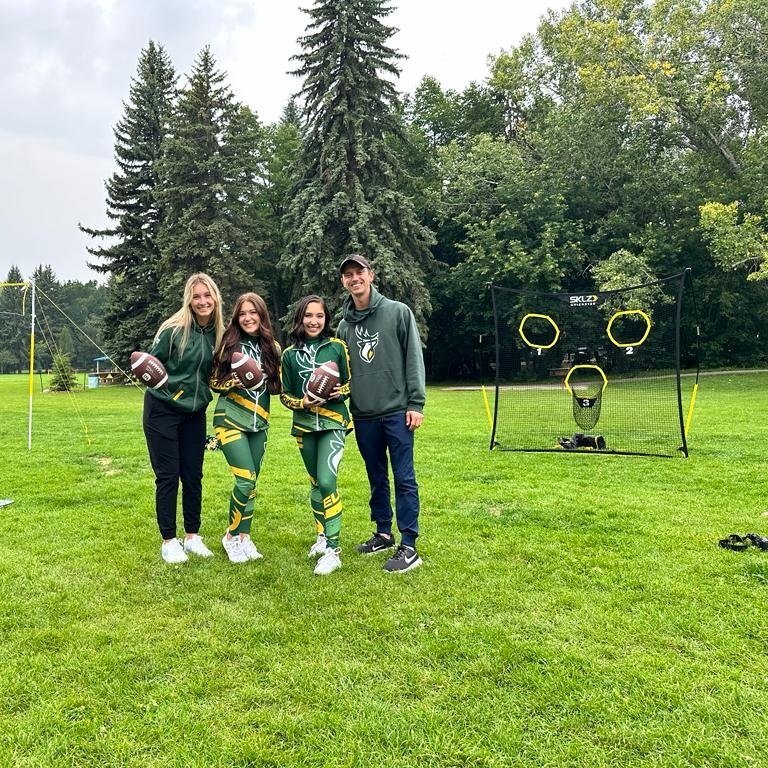  Four members of the Edmonton Elks Cheer team stand together on a green lawn with sport nets behind them.  