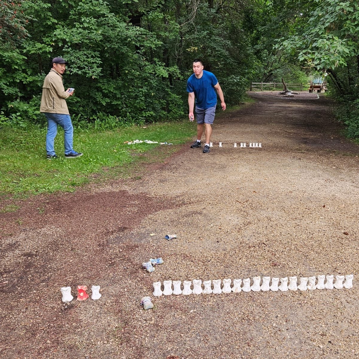  Two men are playing a lawn game on a dirt path. One man is about to throw a bone.  