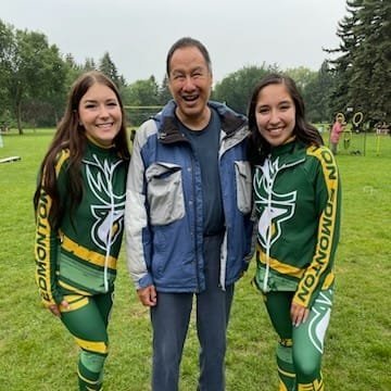  A man stands between two Edmonton Elks Cheer Team members. All three are smiling.  