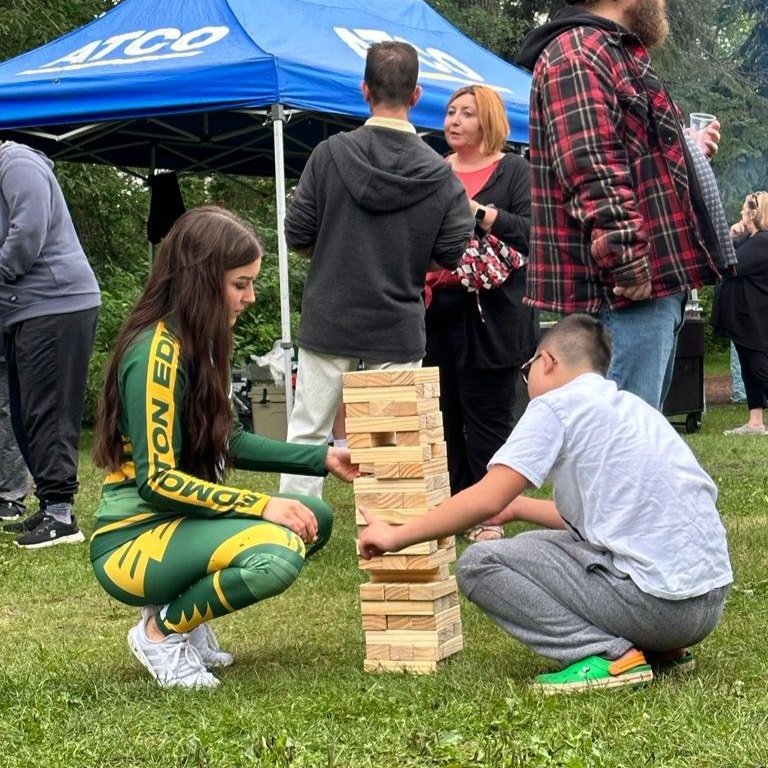  An Edmonton Elks Cheer Team member plays Jenga with a young boy. They are both pulling blocks from the tower.  