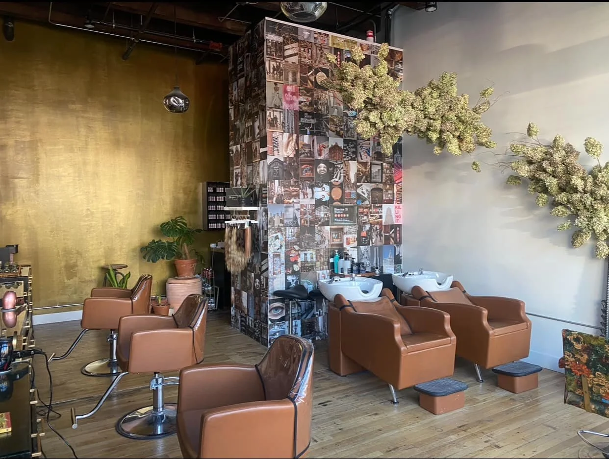 Interior of a hair salon with brown leather chairs, washing stations, and wall art collage.
