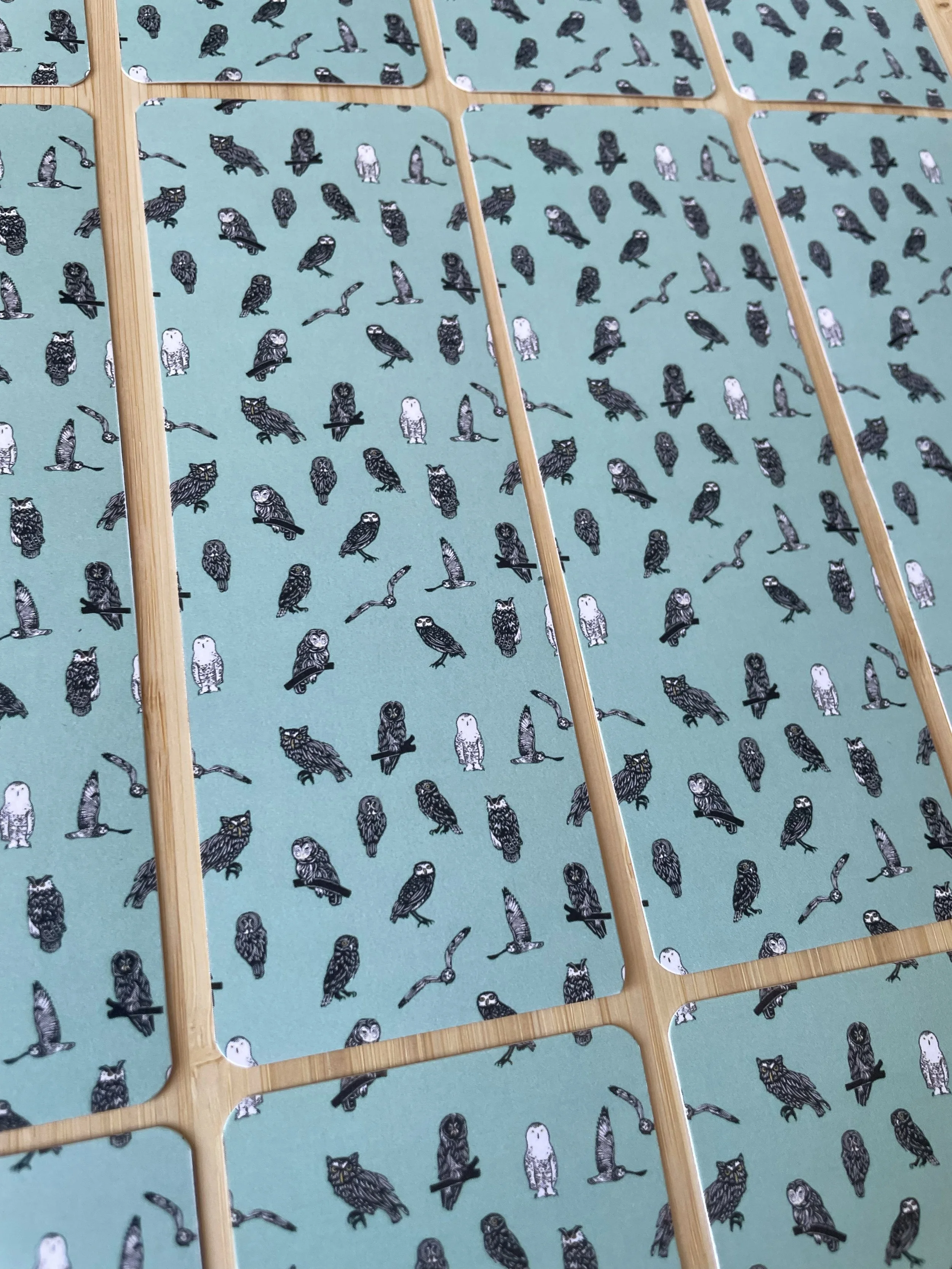 A grid of teal bookmarks with mini owls sit on a wooden background.