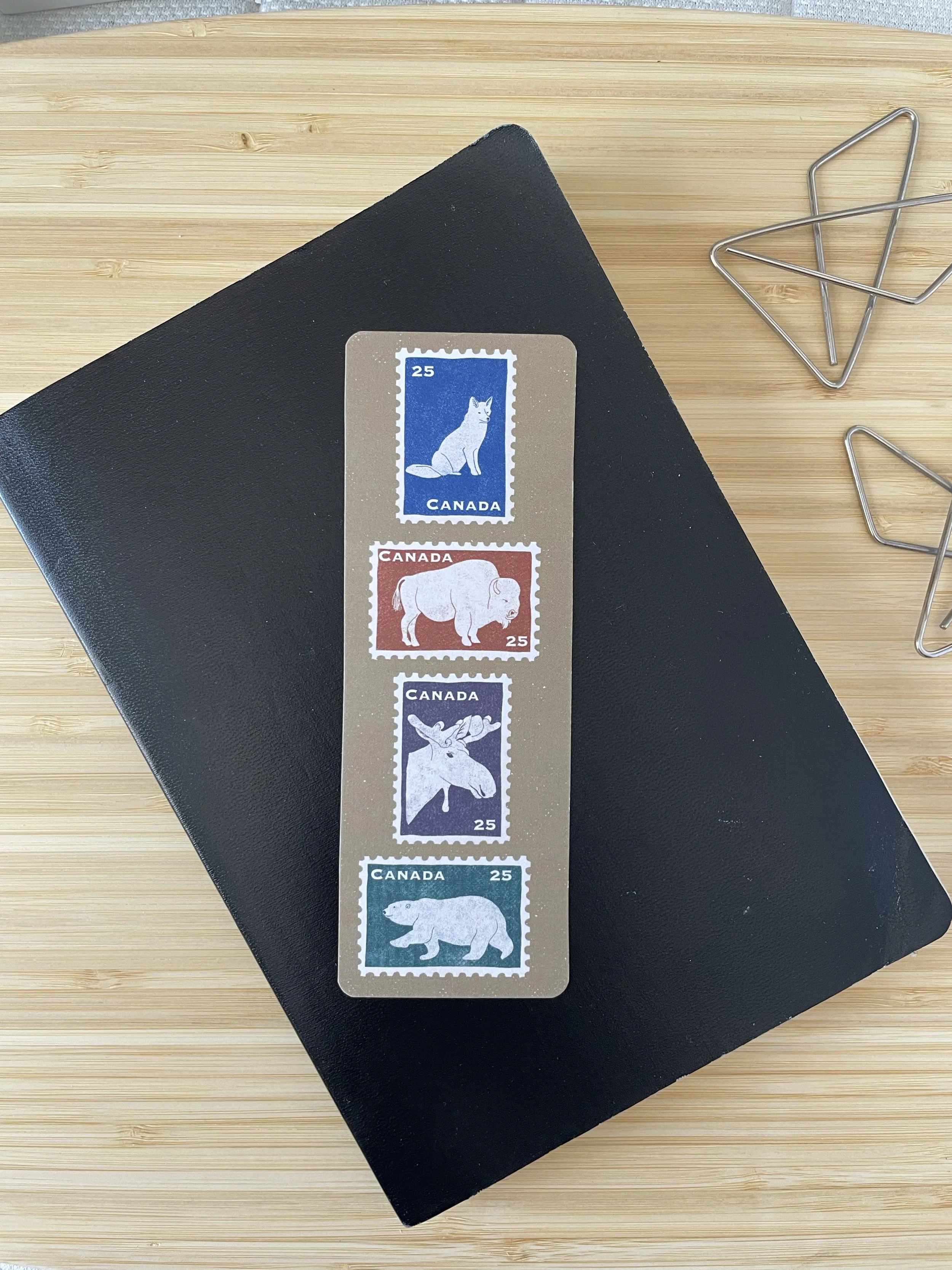A bookmark featuring 4 iconic Canadian mammals sits across a leather journal.