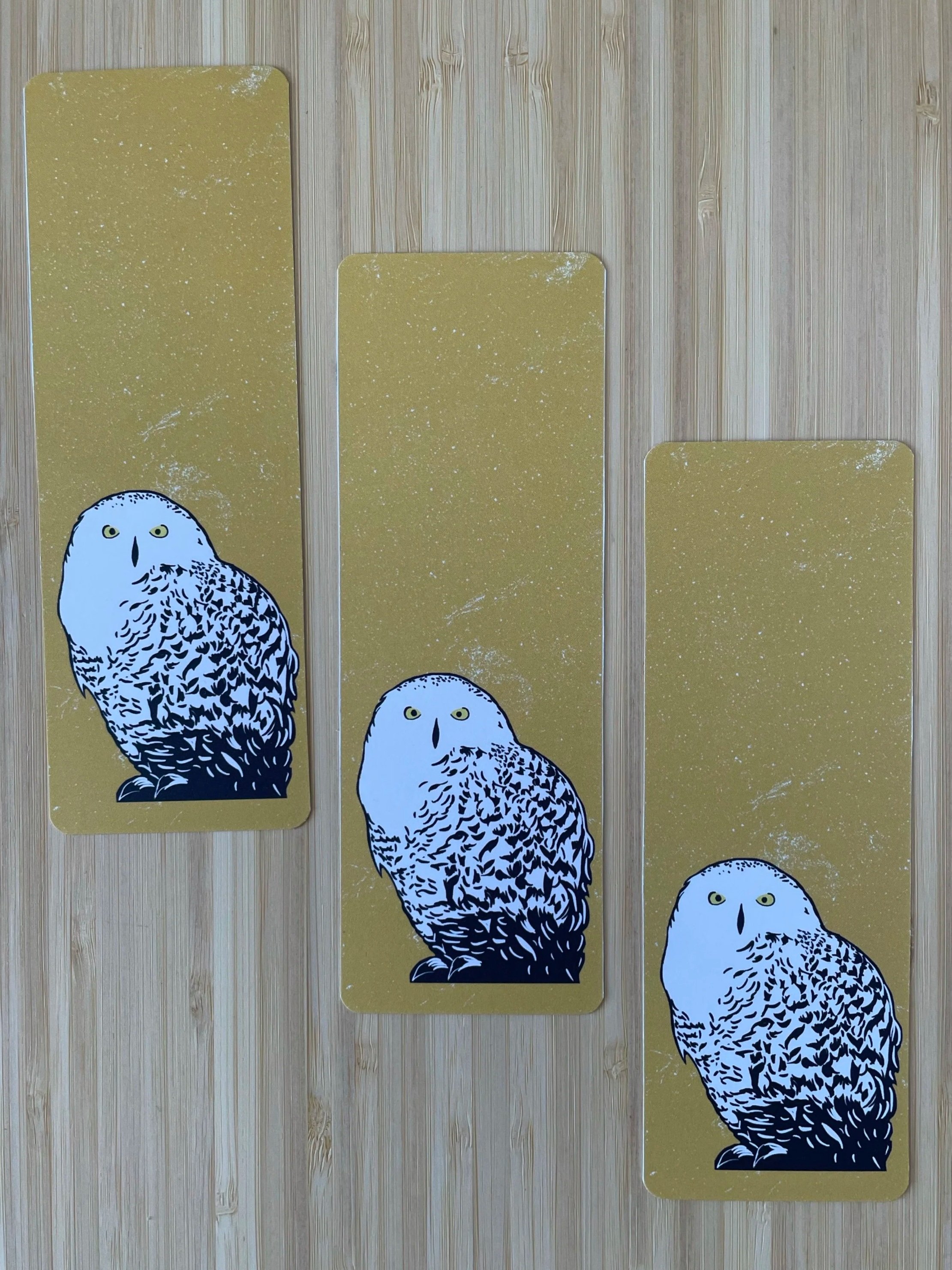 A trio of snowy owl bookmarks sits atop of a wooden surface in a diagonal line.