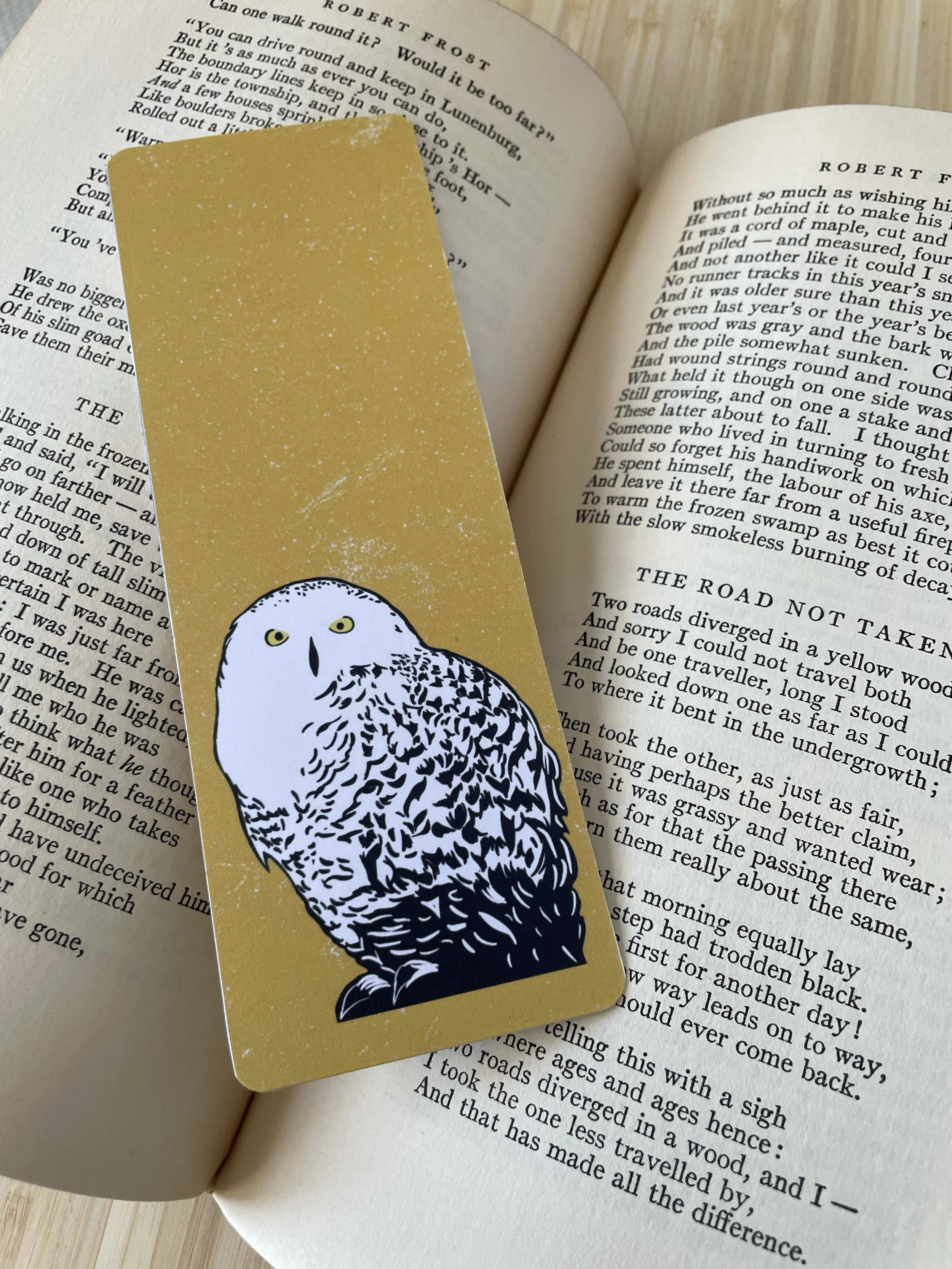 A yellow bookmark featuring a snowy owl sits on the pages of an open book,