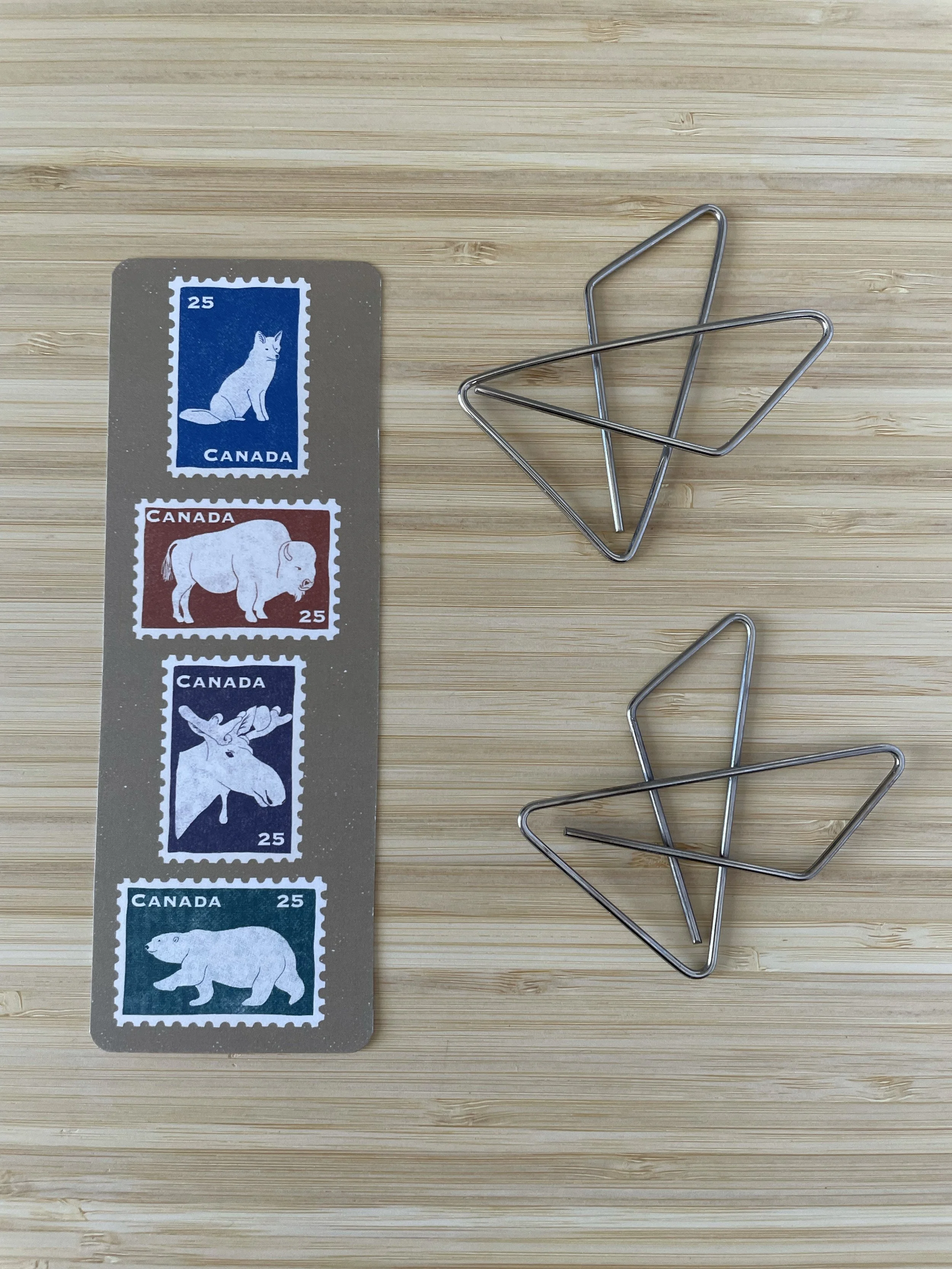 A bookmark sits atop of a wooden surface beside two large paper clips.